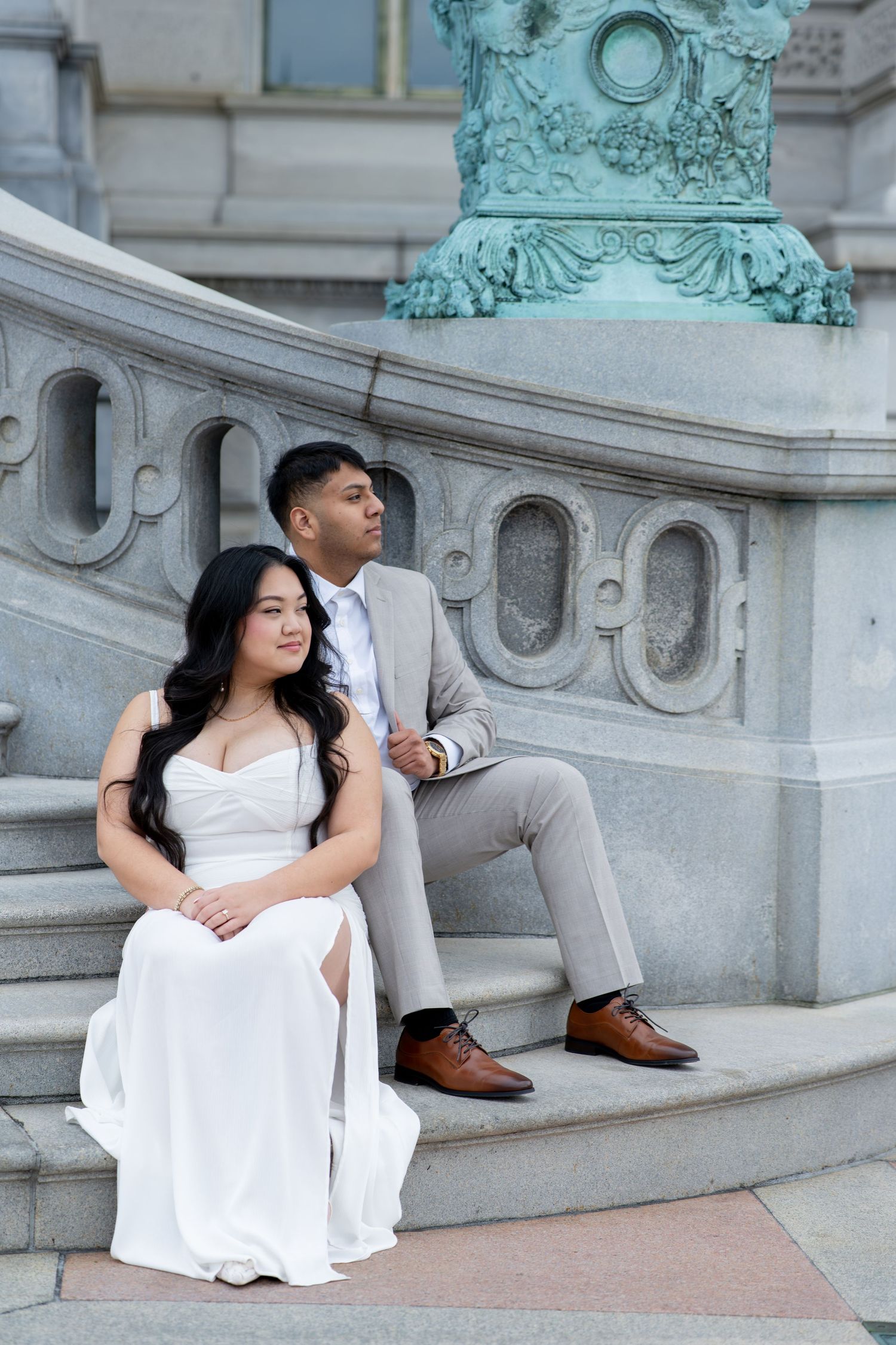 Bride and groom sitting on ornate stone steps beside a bronze statue.