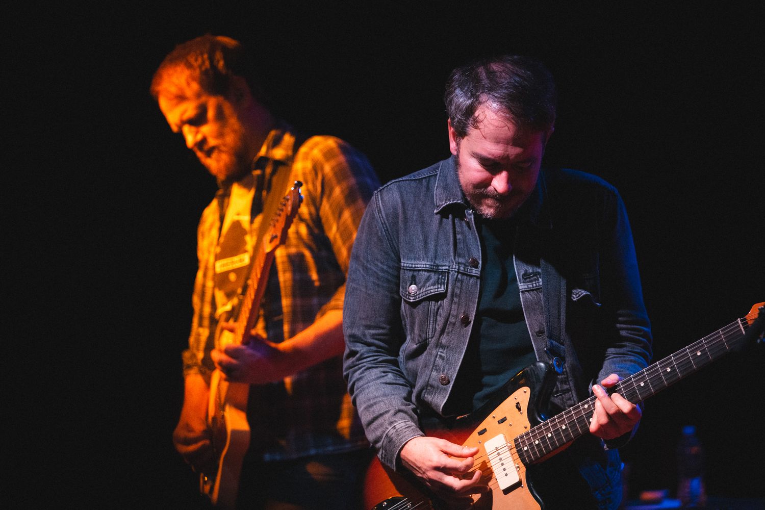 Guitar players perform on stage with moody blue and orange stage lighting.