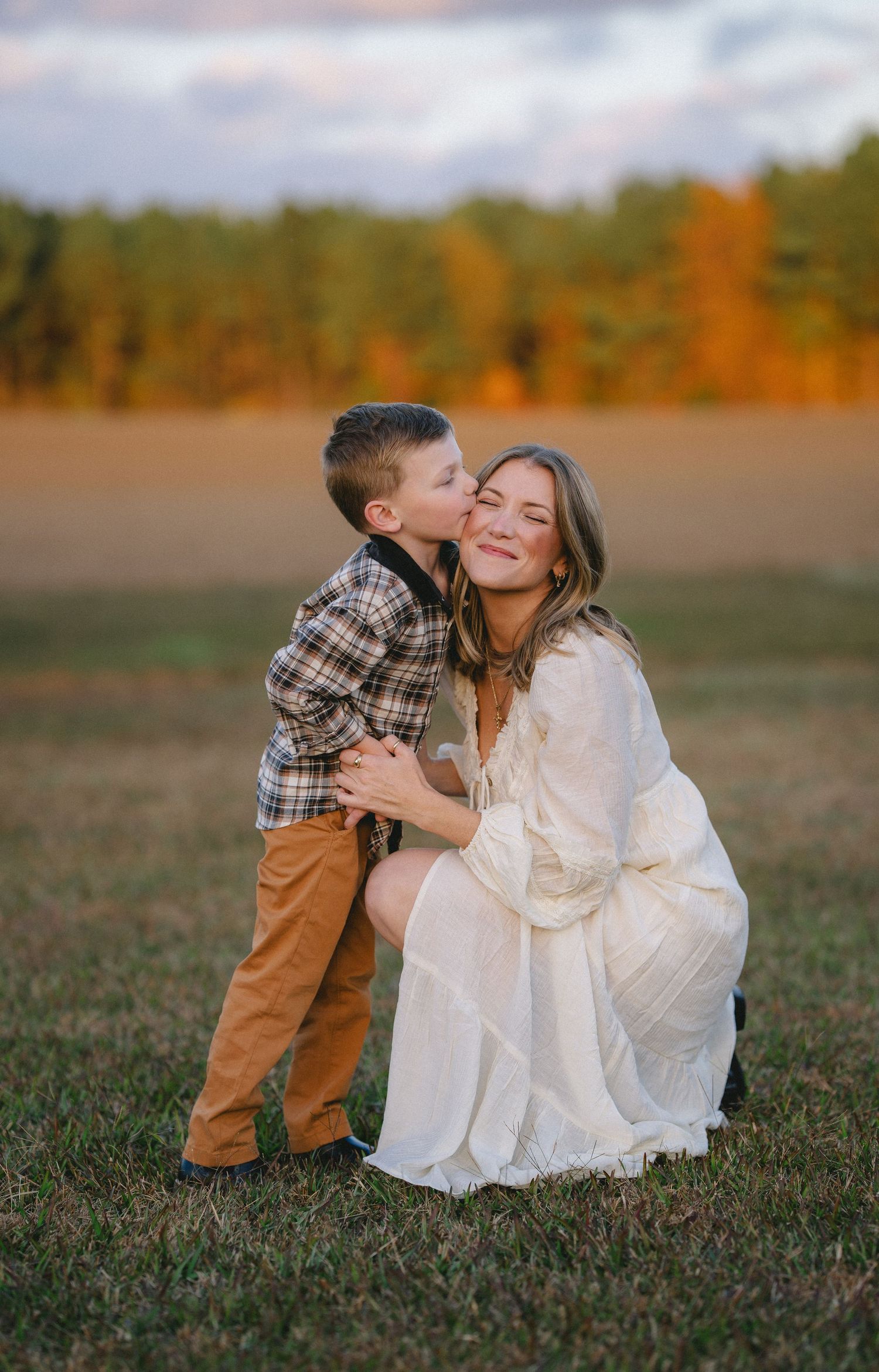 A sweet moment shared between parent and child in a grassy field during autumn with orange foliage in the background.