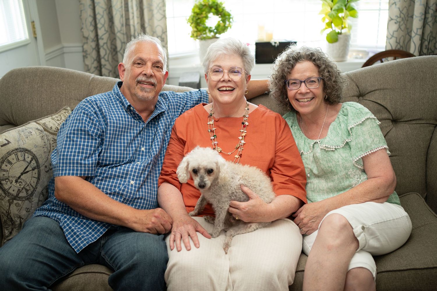 Family group relaxes on a cozy couch with their small white dog.