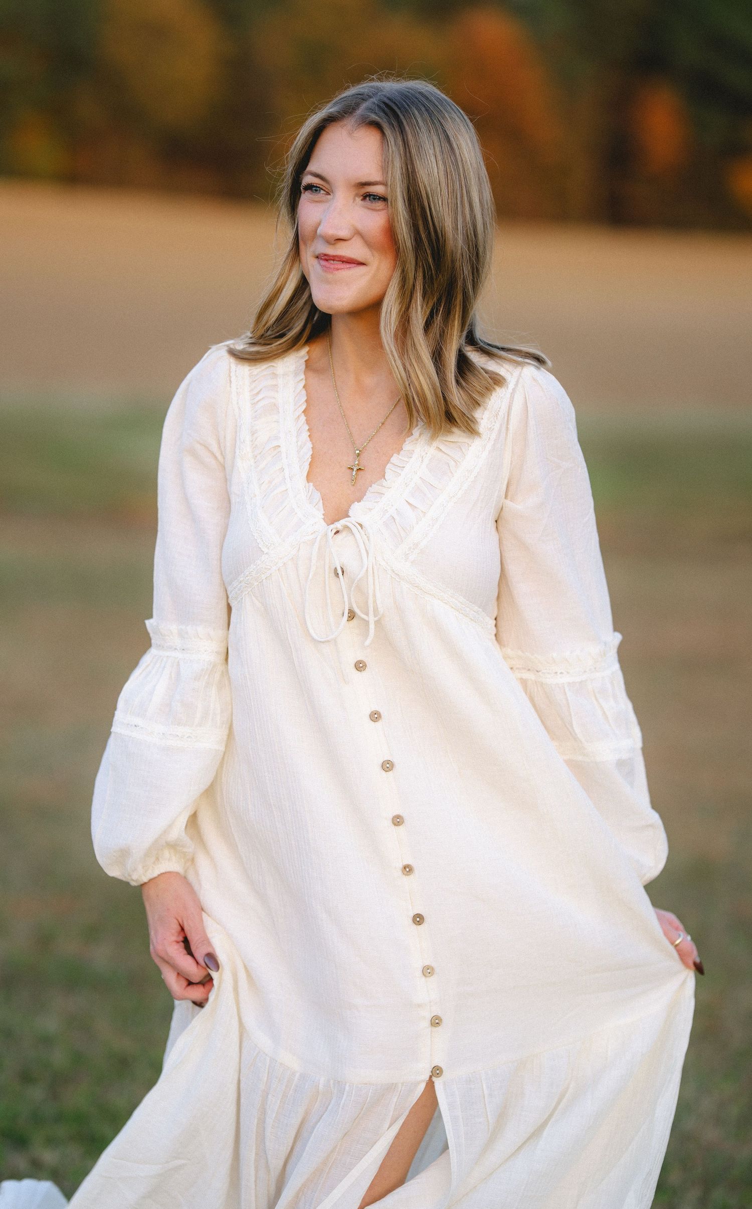Woman in flowing white dress twirls gracefully in an autumn field during golden hour photography session.