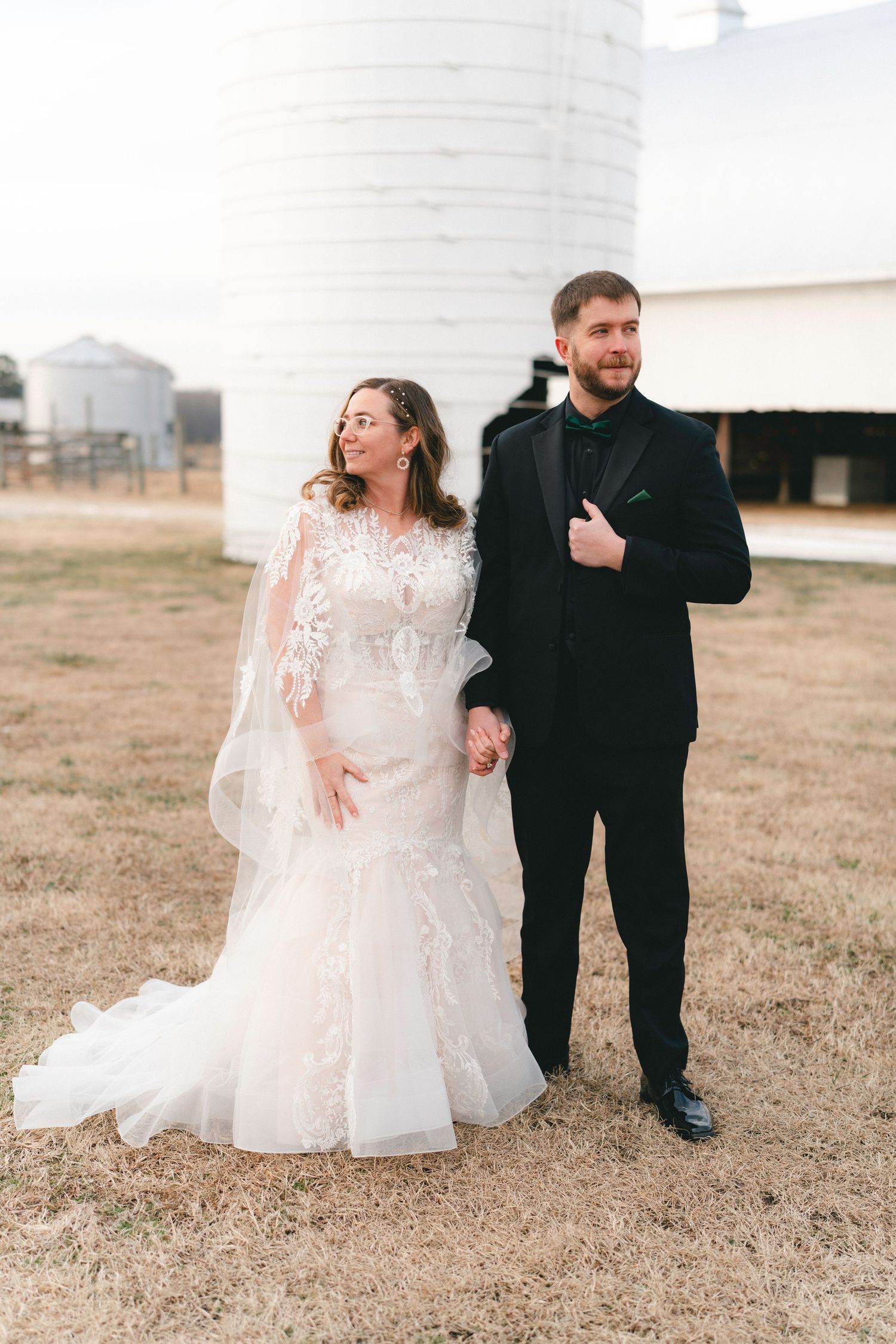 A couple shares joyful moments in a field, with the bride wearing a flowing white dress and the groom in black attire.