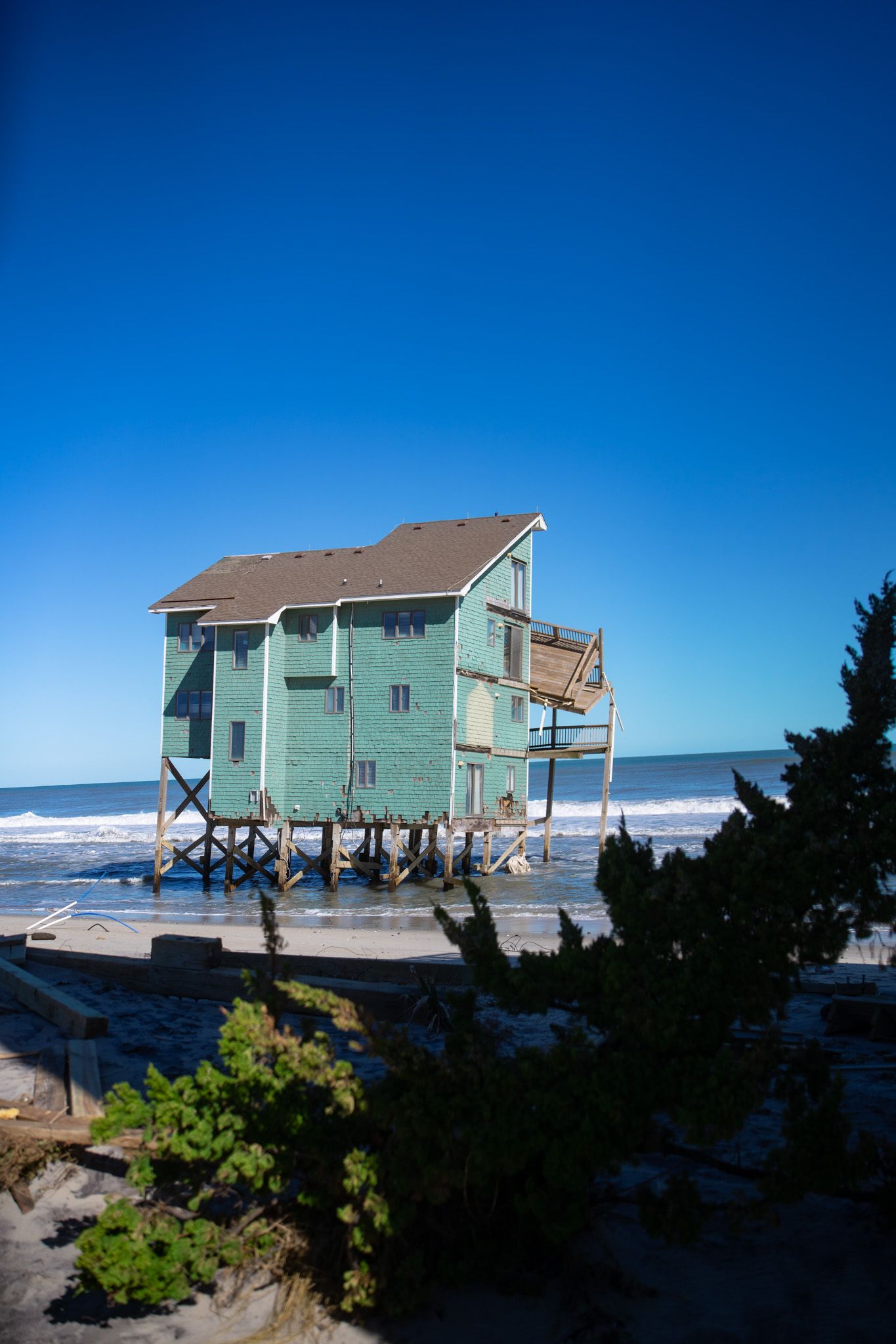 A series of photos showing a coastal beach house on stilts against a bright blue sky and ocean backdrop.