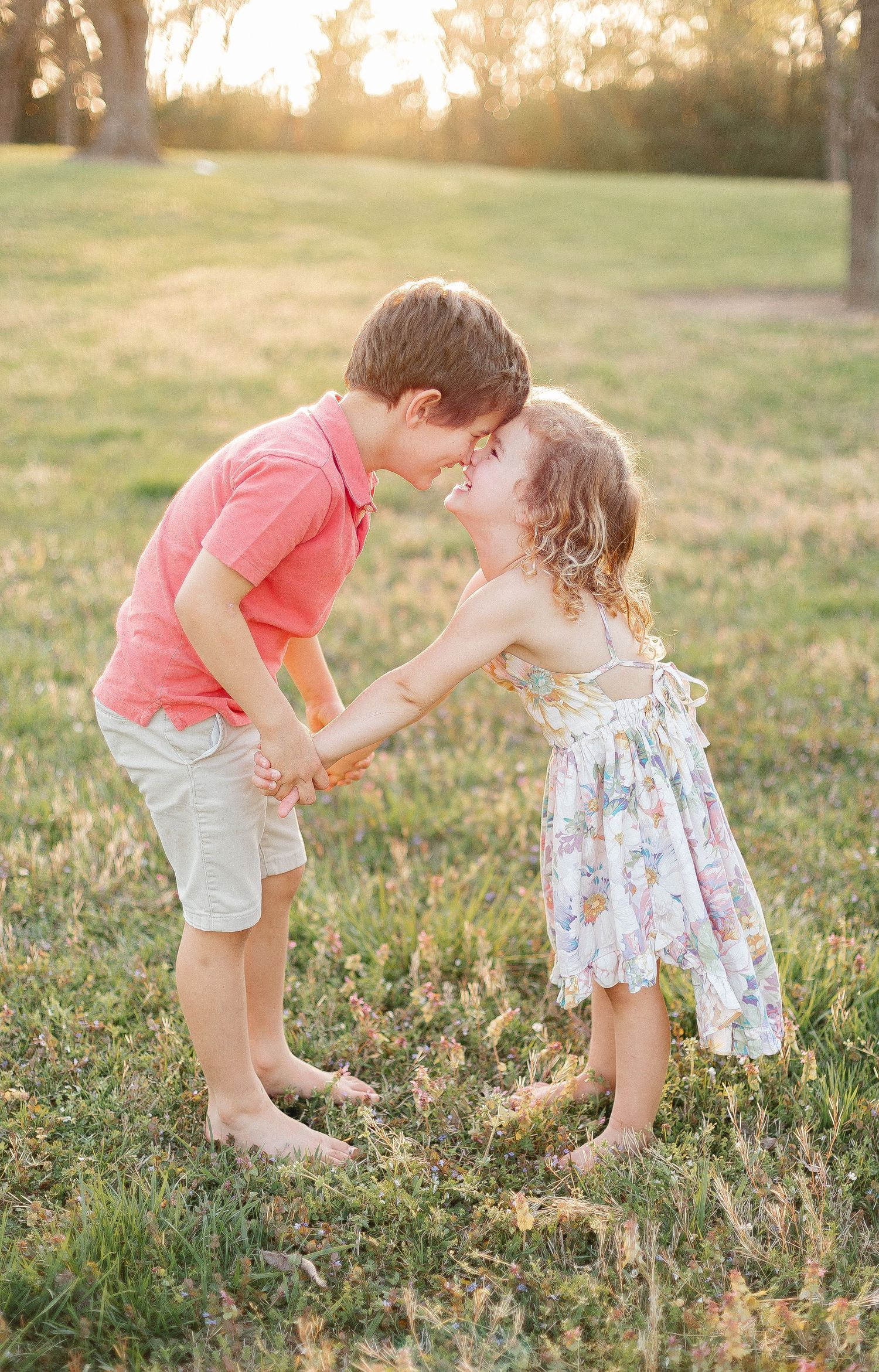Two children in summer outfits share playful moment in sunlit field.