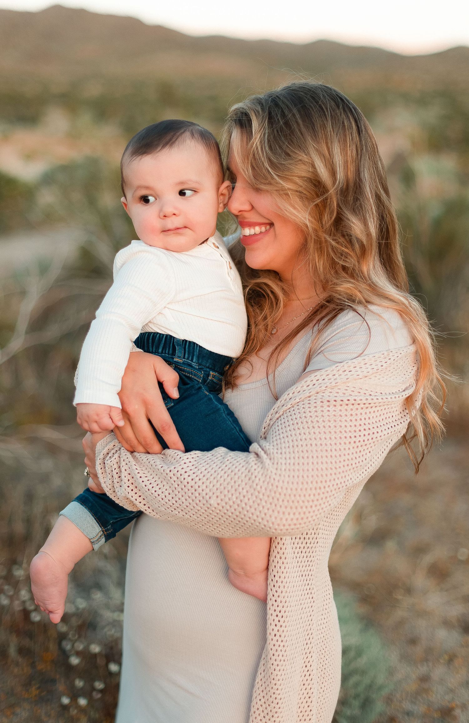 Sweet moment between parent and baby against desert landscape at sunset.