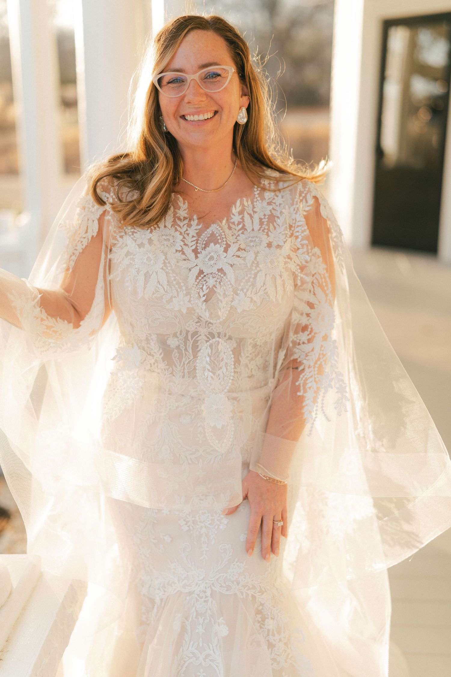 Bride in delicate lace wedding dress poses in glowing natural sunlight.