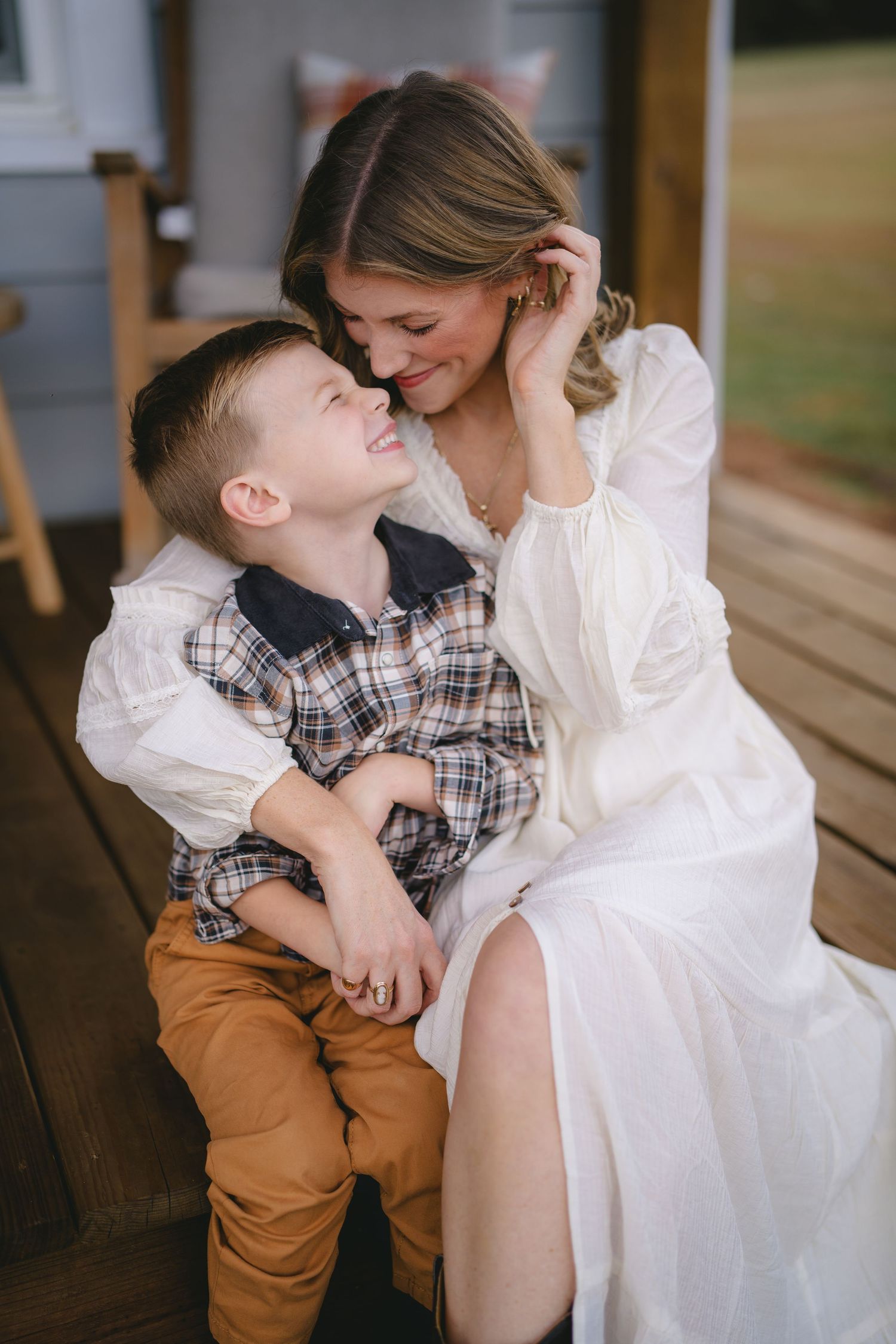 Sweet candid moments between a young child in plaid and someone in white on a wooden porch.