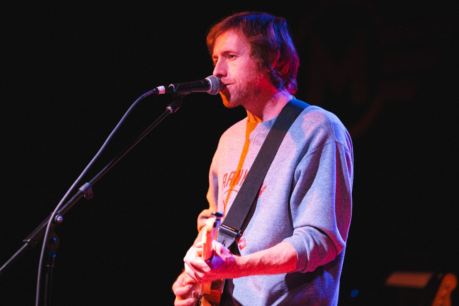 Concert performer plays guitar under dramatic stage lighting.