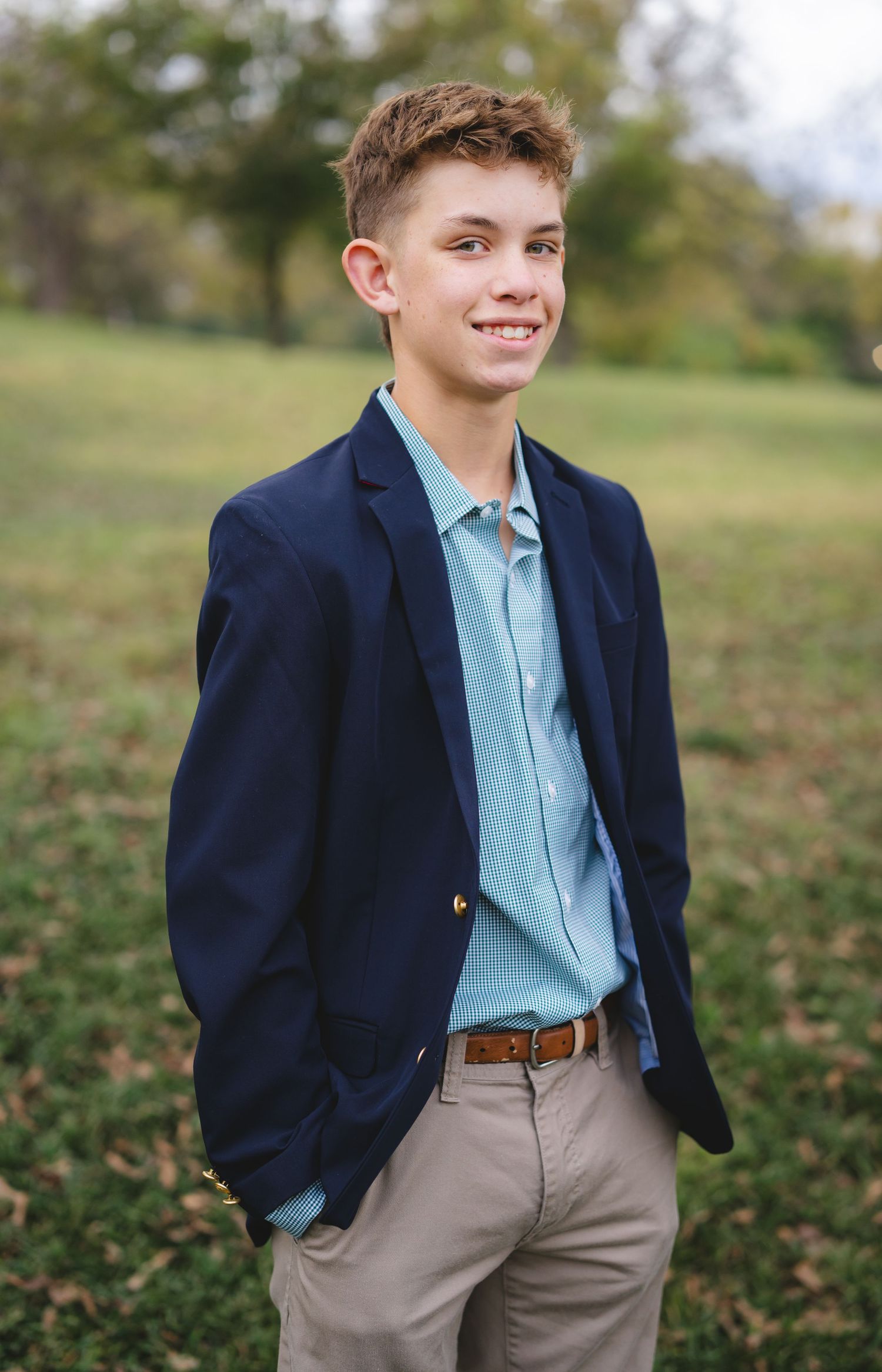 Young person in navy blazer and khakis poses confidently outdoors during fall season.