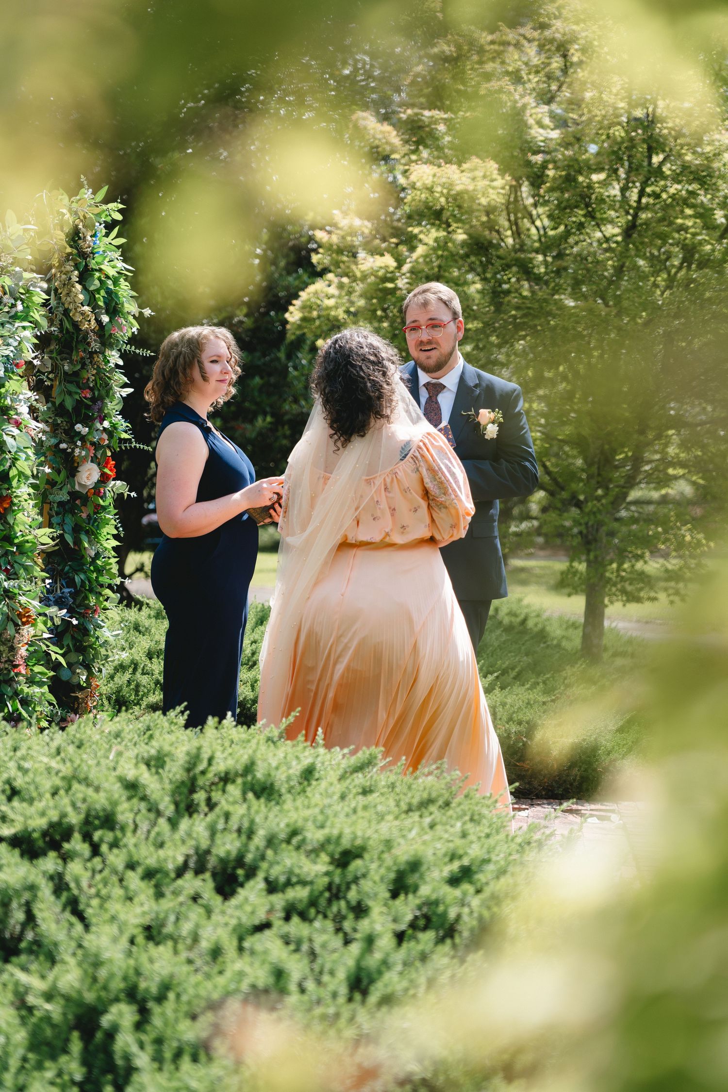 A wedding ceremony takes place in a lush garden setting with soft natural lighting.