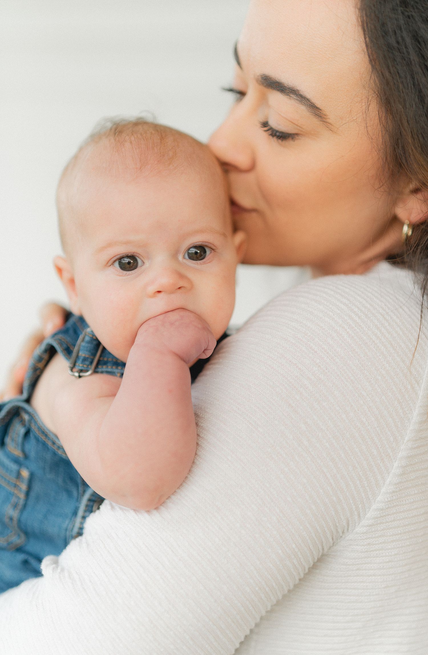 Tender moment between parent and baby in white sweater and denim overalls.