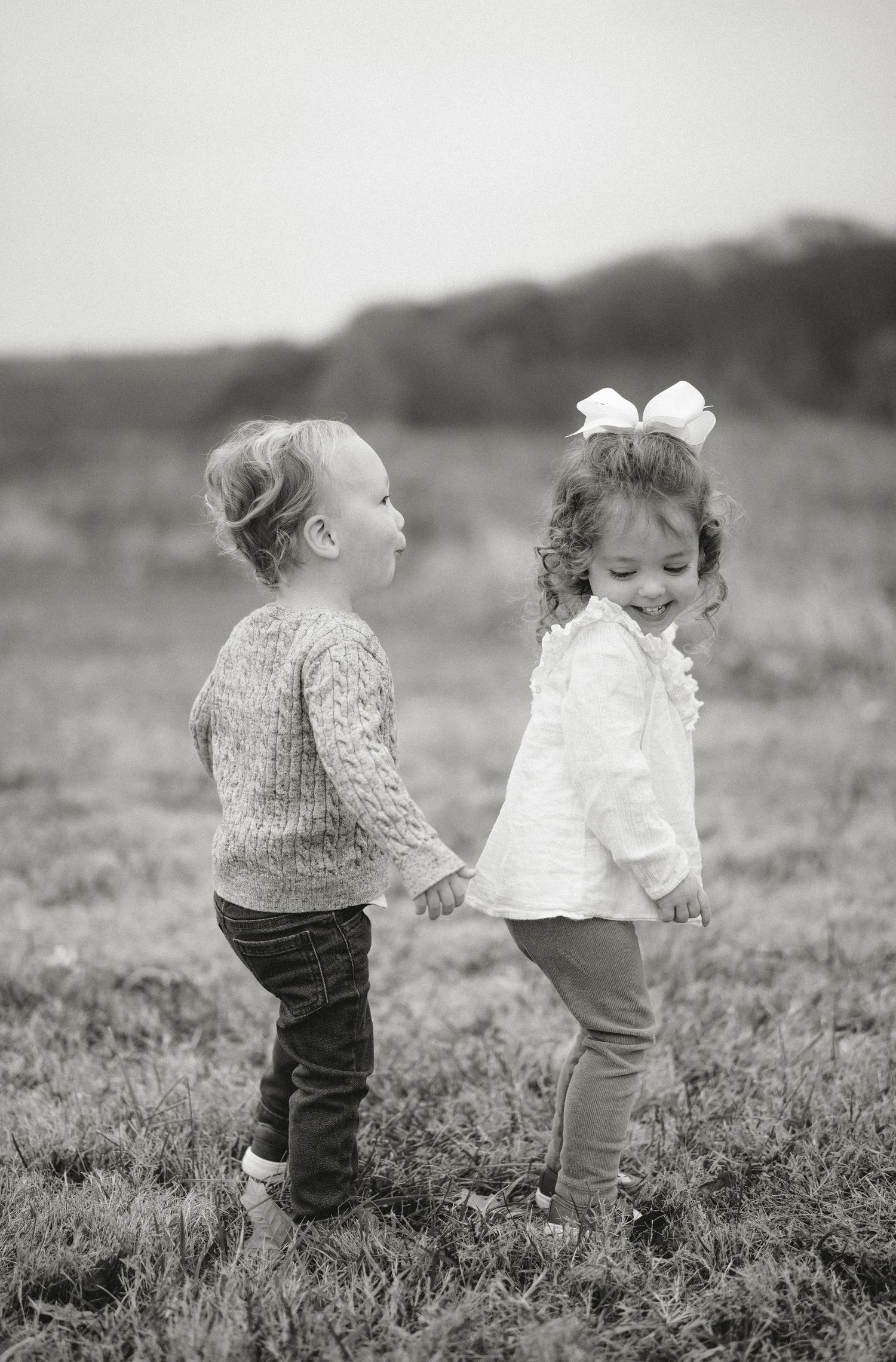 Two toddlers in sweaters interact playfully in a black and white photograph.
