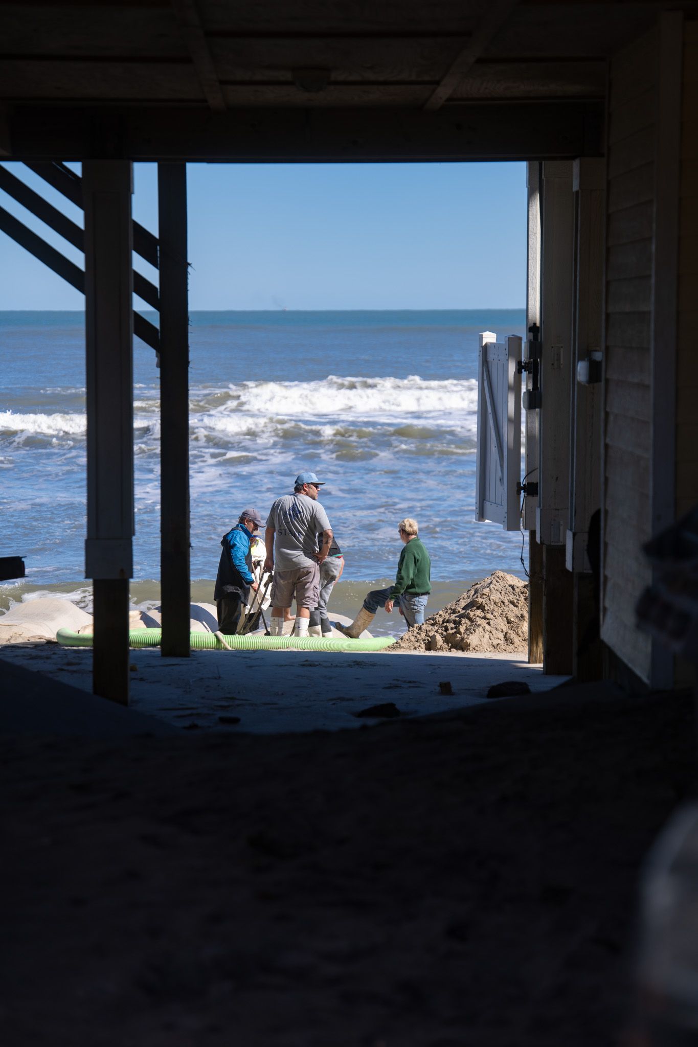 View of beach and ocean waves through dark pillars of beach house. Buxton, North Carolina. Outer Banks.