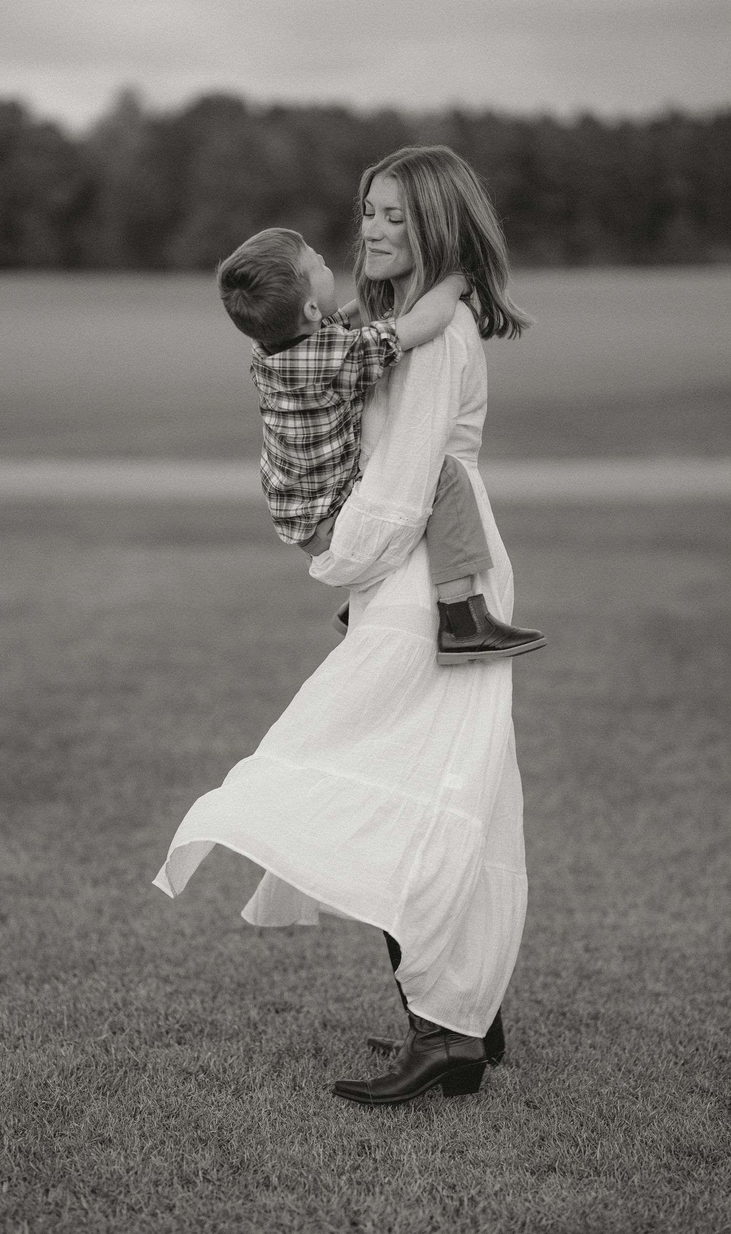 A tender black and white portrait of family members dancing in a grassy field.