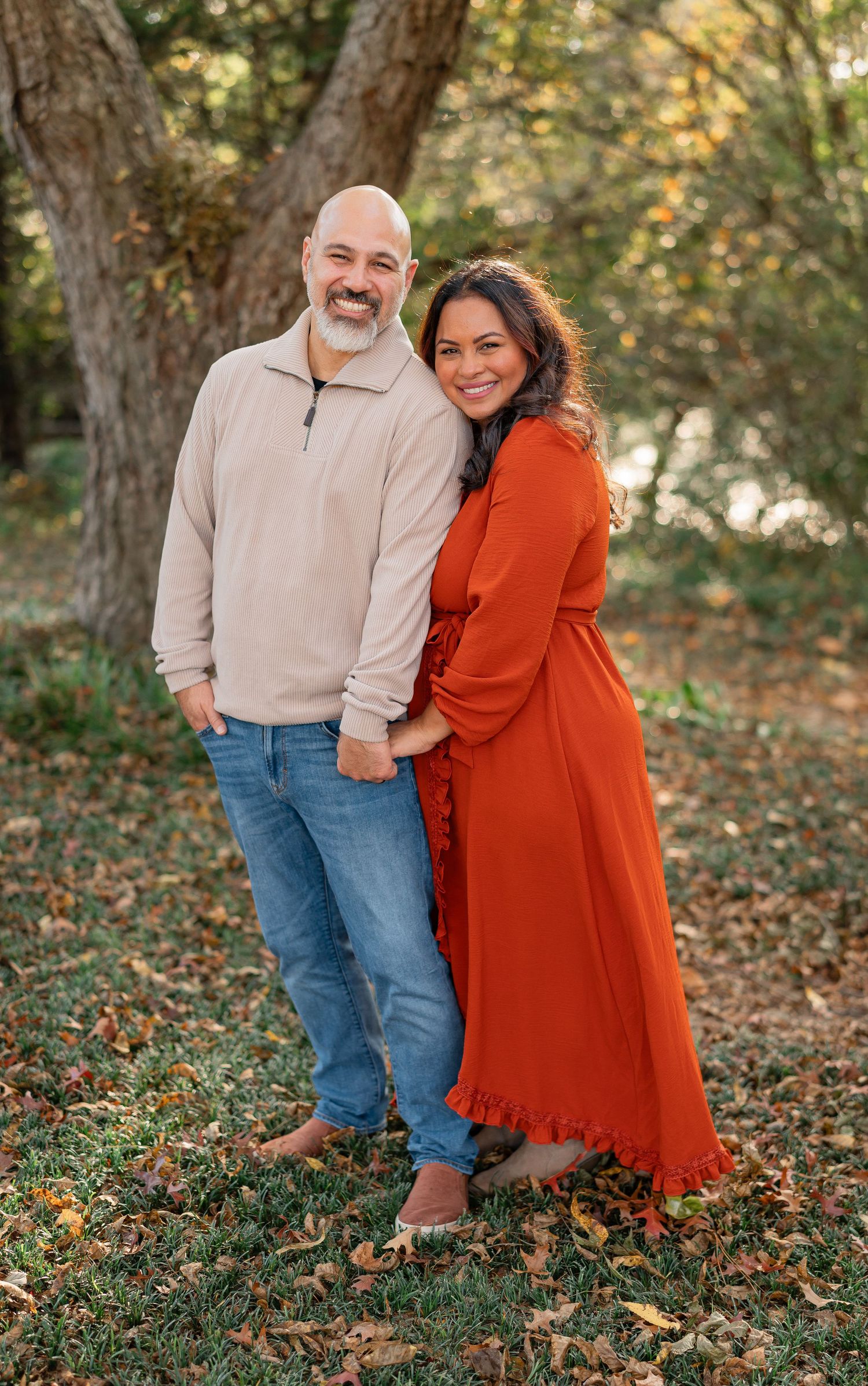 A couple poses for heartwarming fall photos on grass with fallen leaves, wearing red and beige casual attire.