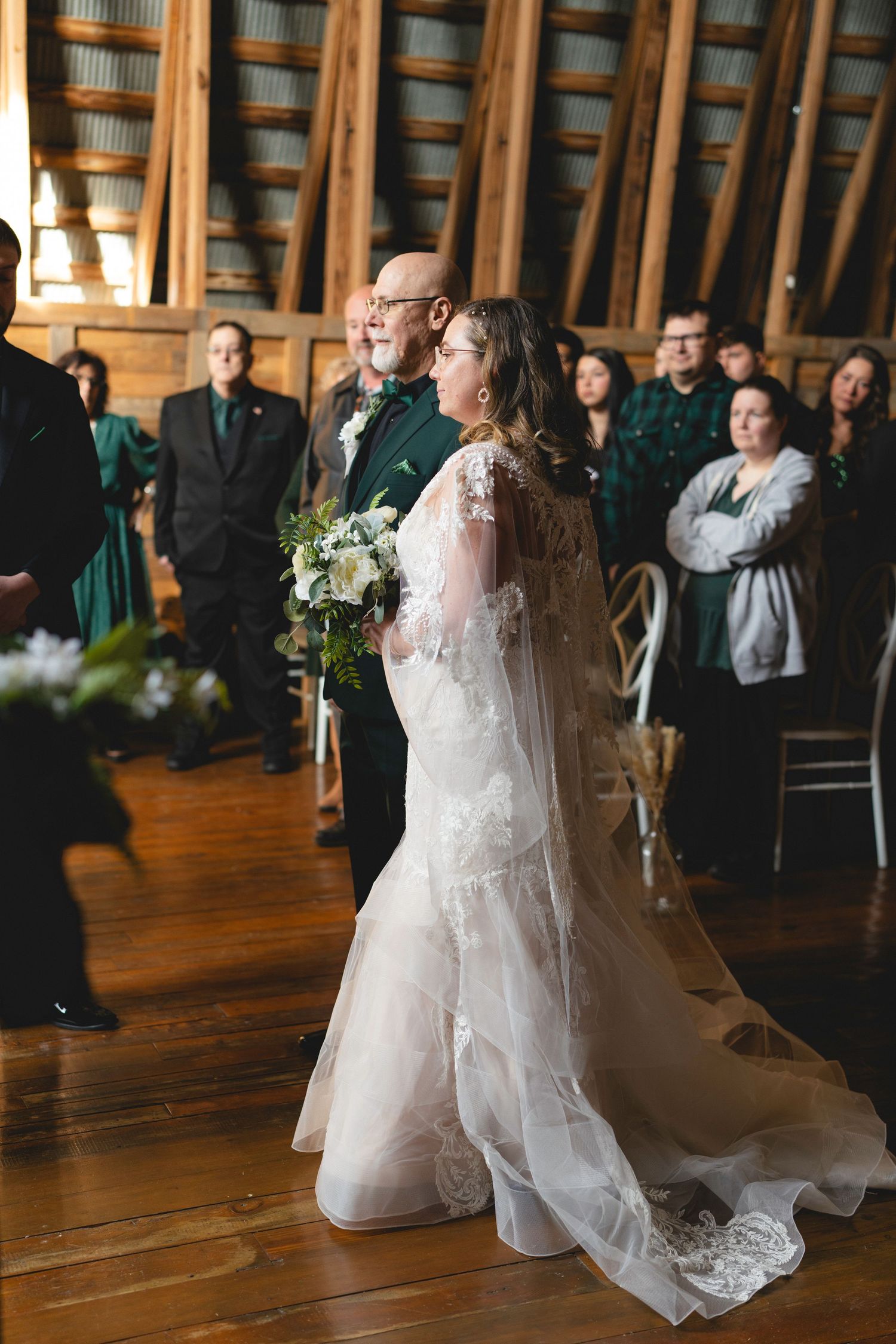 A couple shares their first dance at a rustic wooden venue while wedding guests look on from the sidelines.