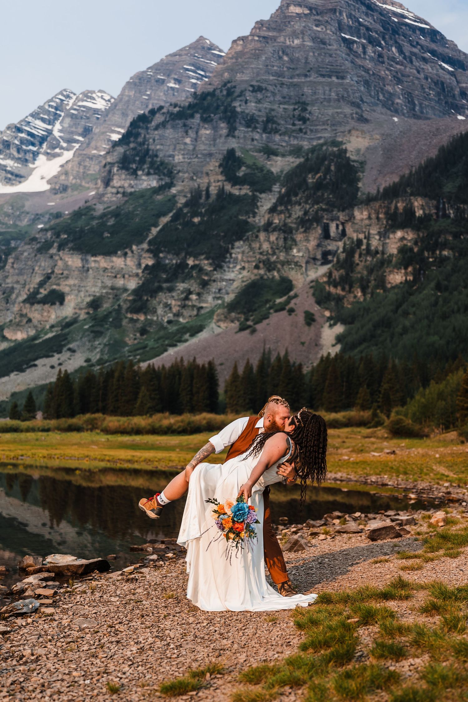 Groom dips bride in romantic kiss near Maroon Bells lake with snow-capped peaks behind them.