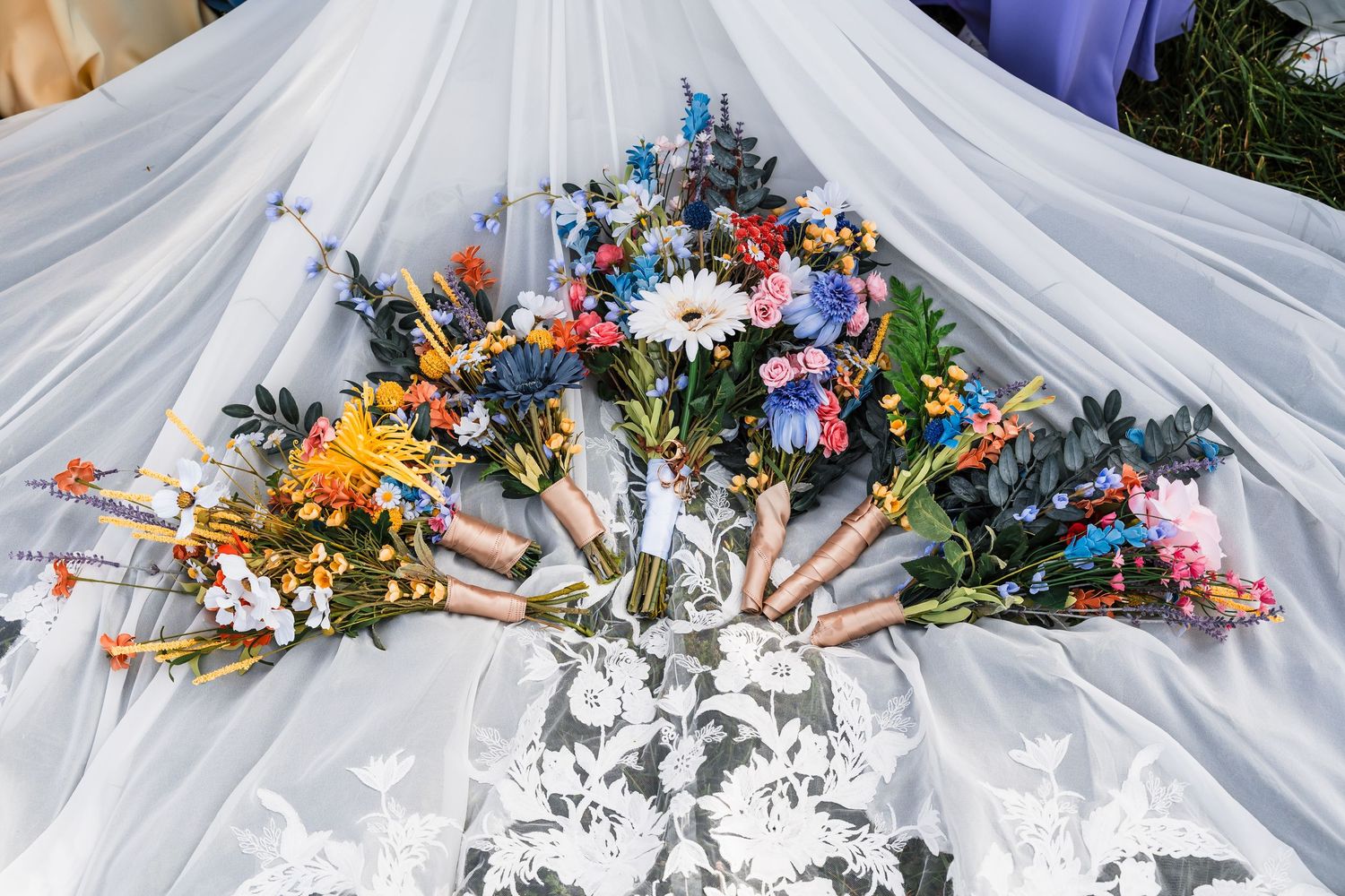 Colorful wildflower wedding bouquets arranged on a white lace bridal veil with blue and pink blooms.