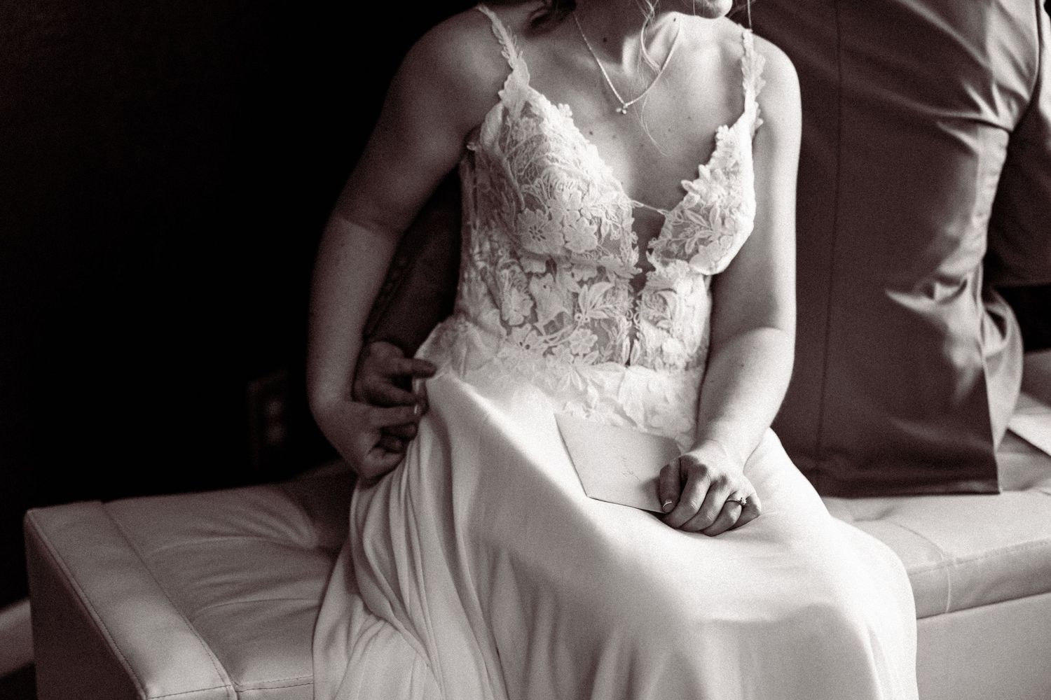 Black and white close-up of bride in elegant lace wedding gown seated gracefully.