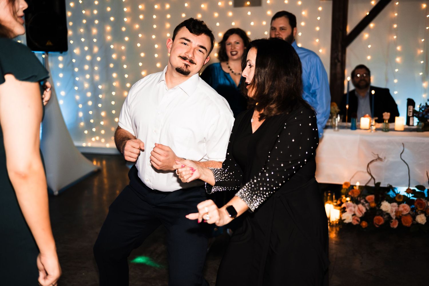 A dancing couple enjoys a lively moment at a party with string lights in the background.