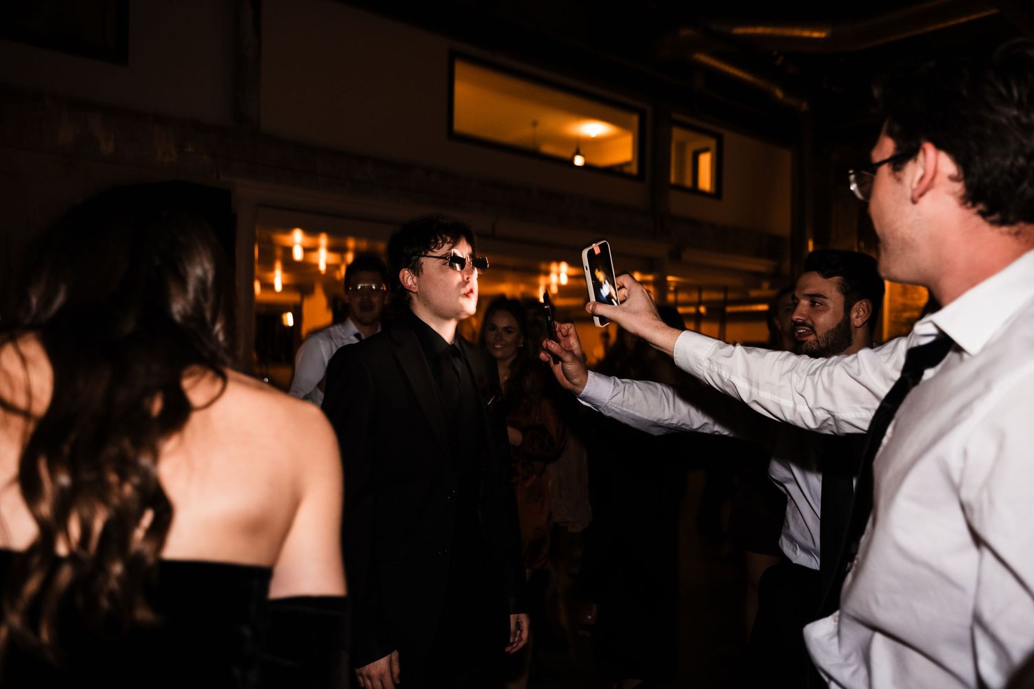 Party guests toasting and celebrating at a lively indoor gathering with ambient lighting.