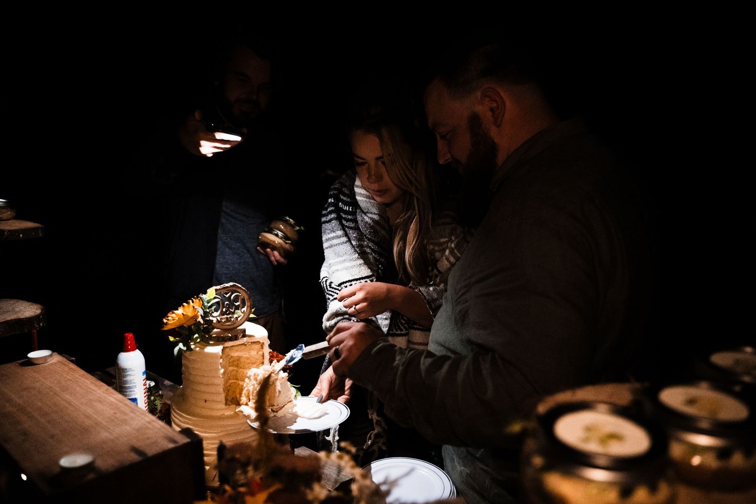 People gather around a dimly lit table with food and drinks in a moody atmospheric setting.