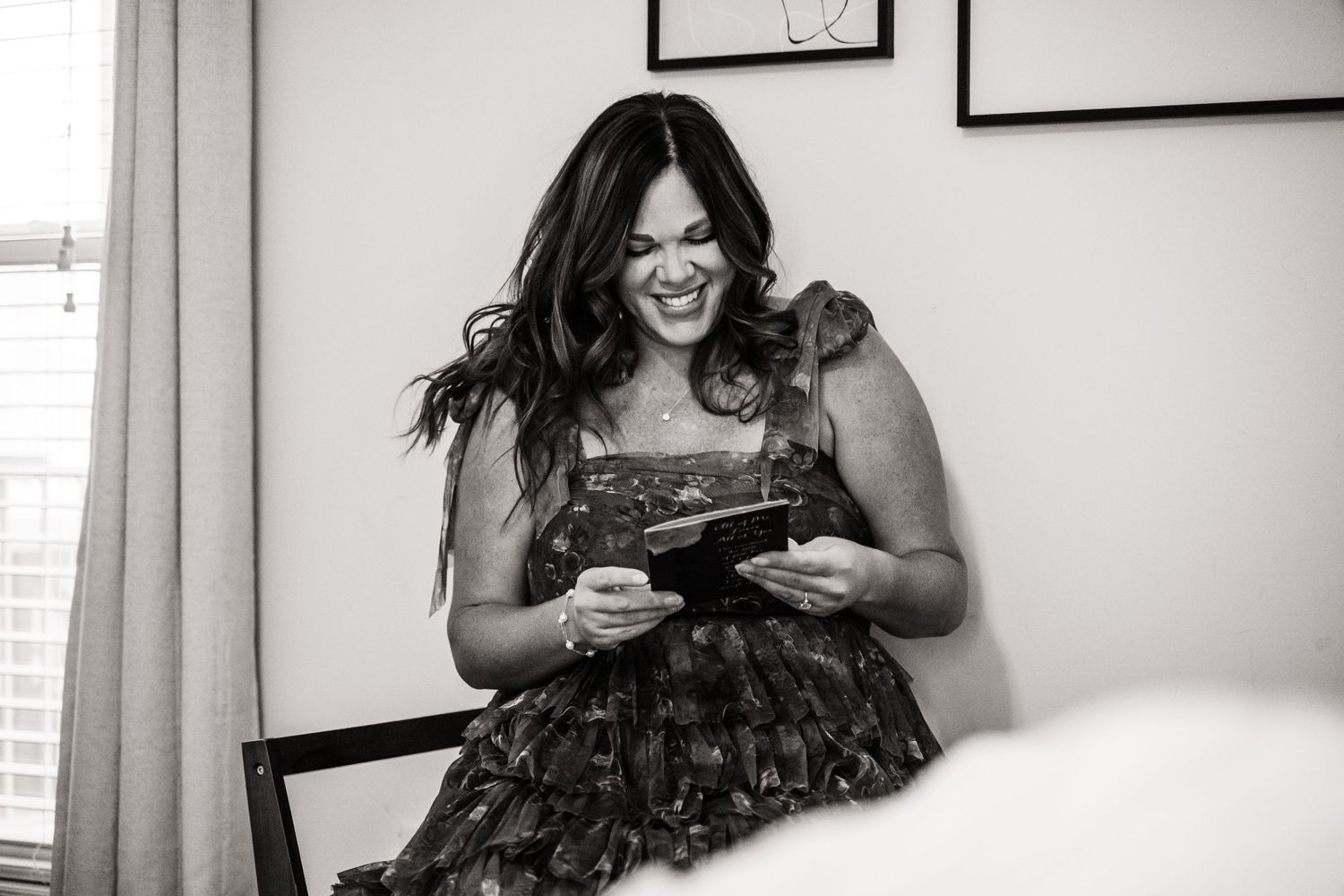 A woman in a patterned dress laughs while writing in a book.