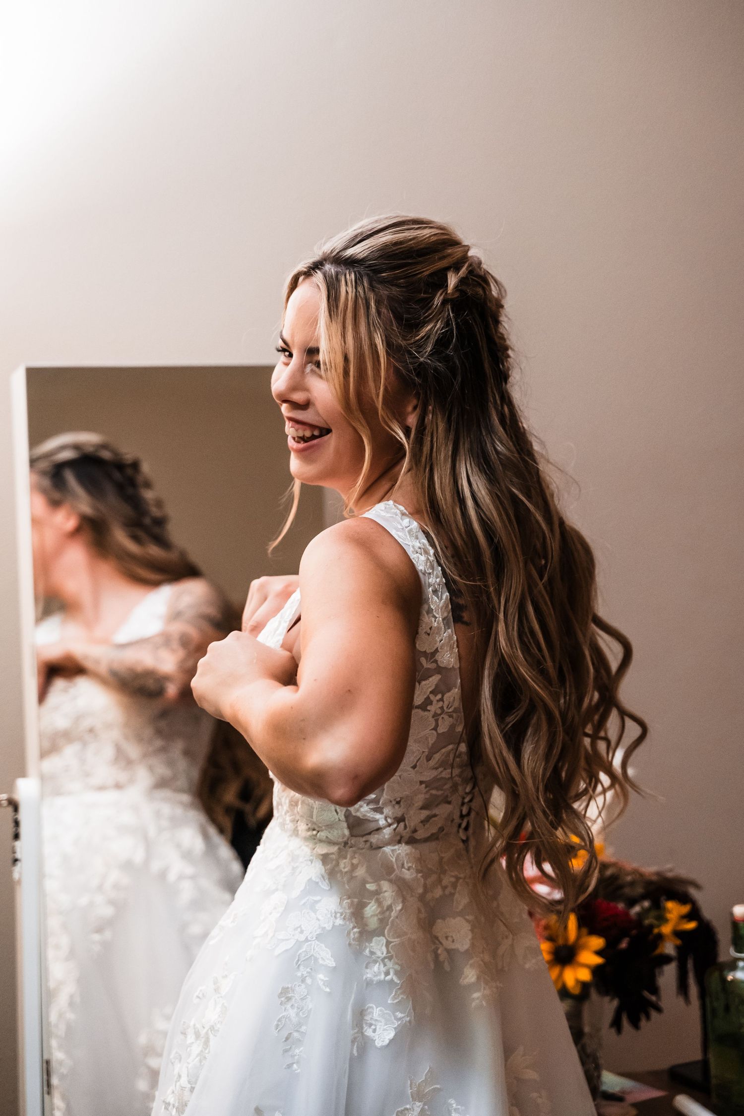 Happy bride wearing a white lace wedding dress laughs while getting ready with her hair styled in long loose waves.
