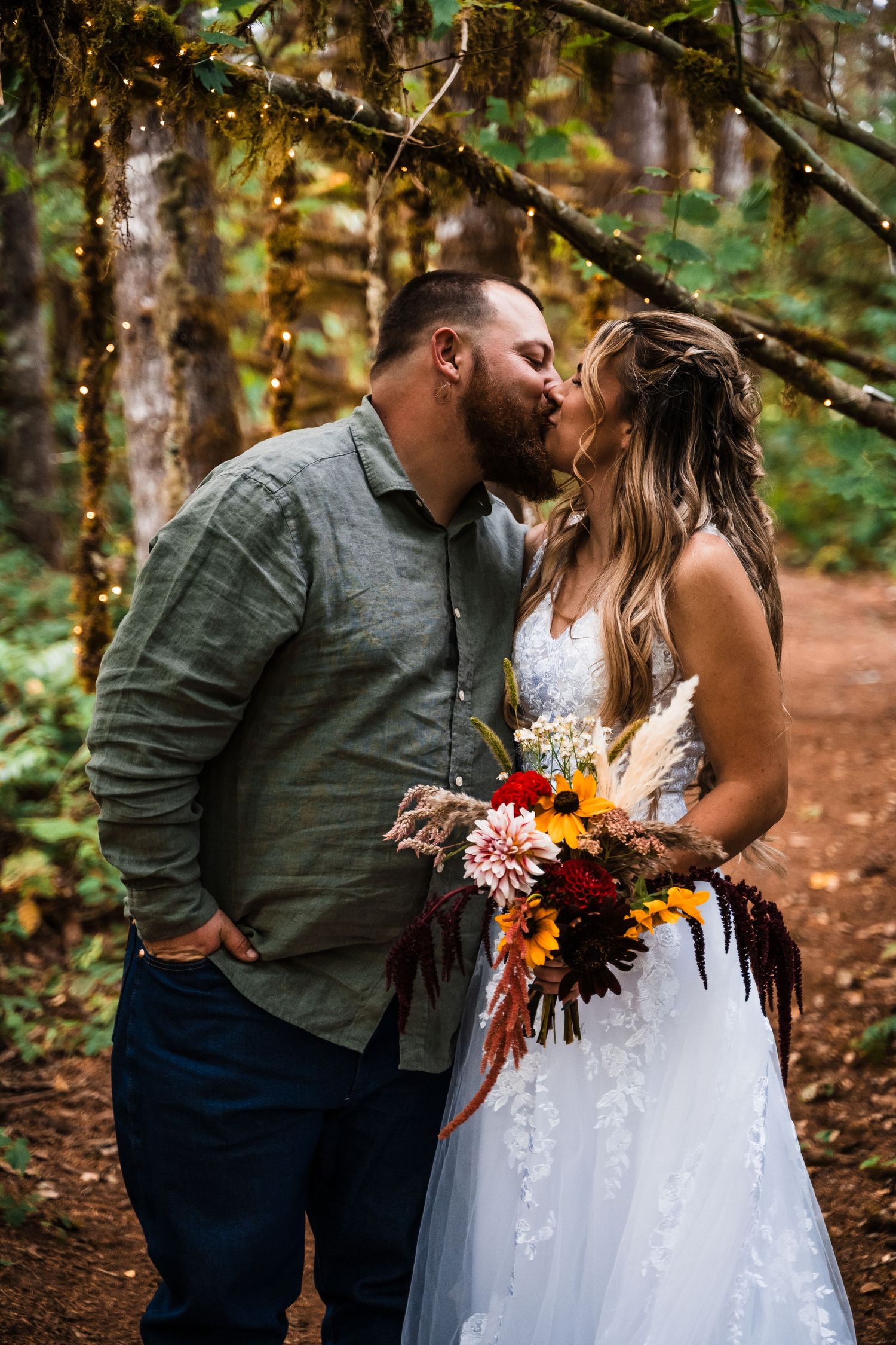 Romantic moment during forest wedding with fall bouquet and moss-covered branches overhead.