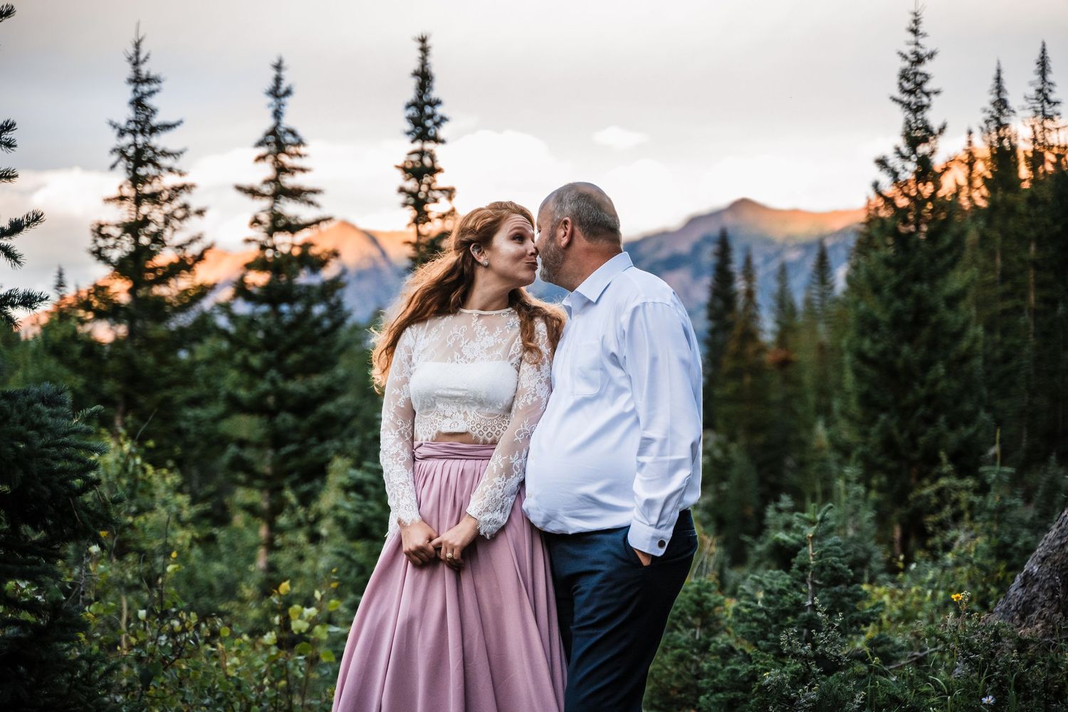 Romantic mountain engagement portrait with evergreen trees at sunset.