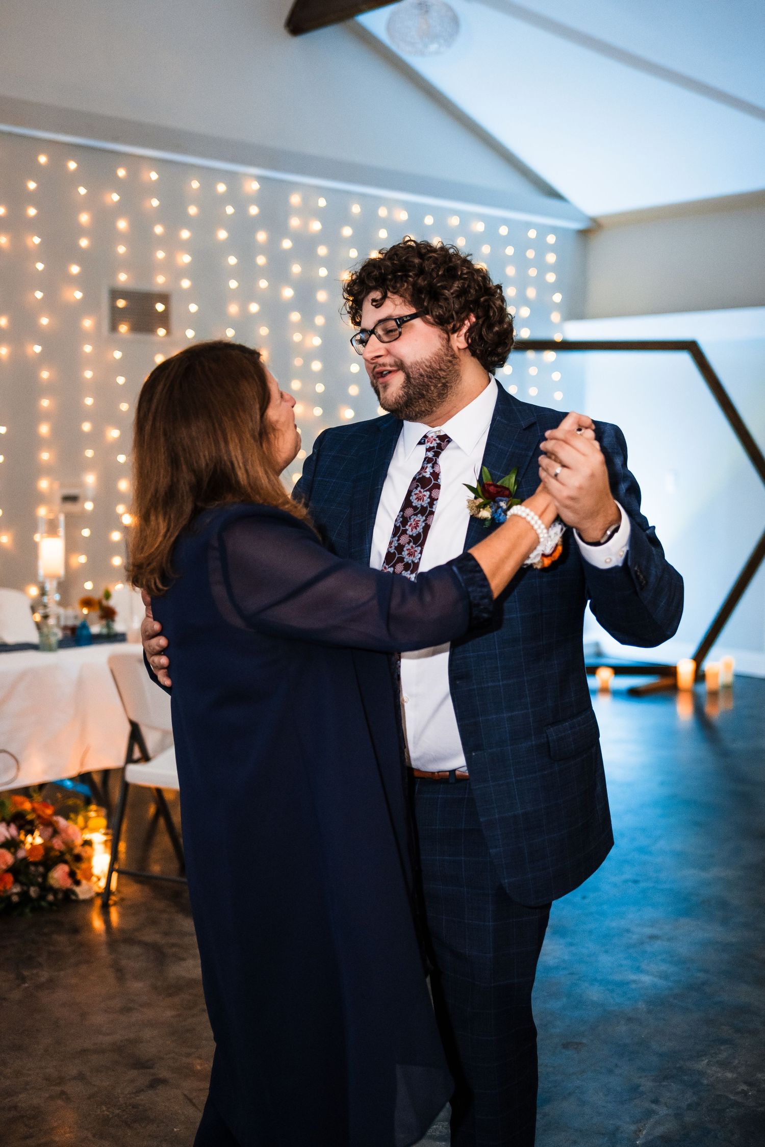 A dancing couple shares a joyful moment at a wedding reception with string lights.