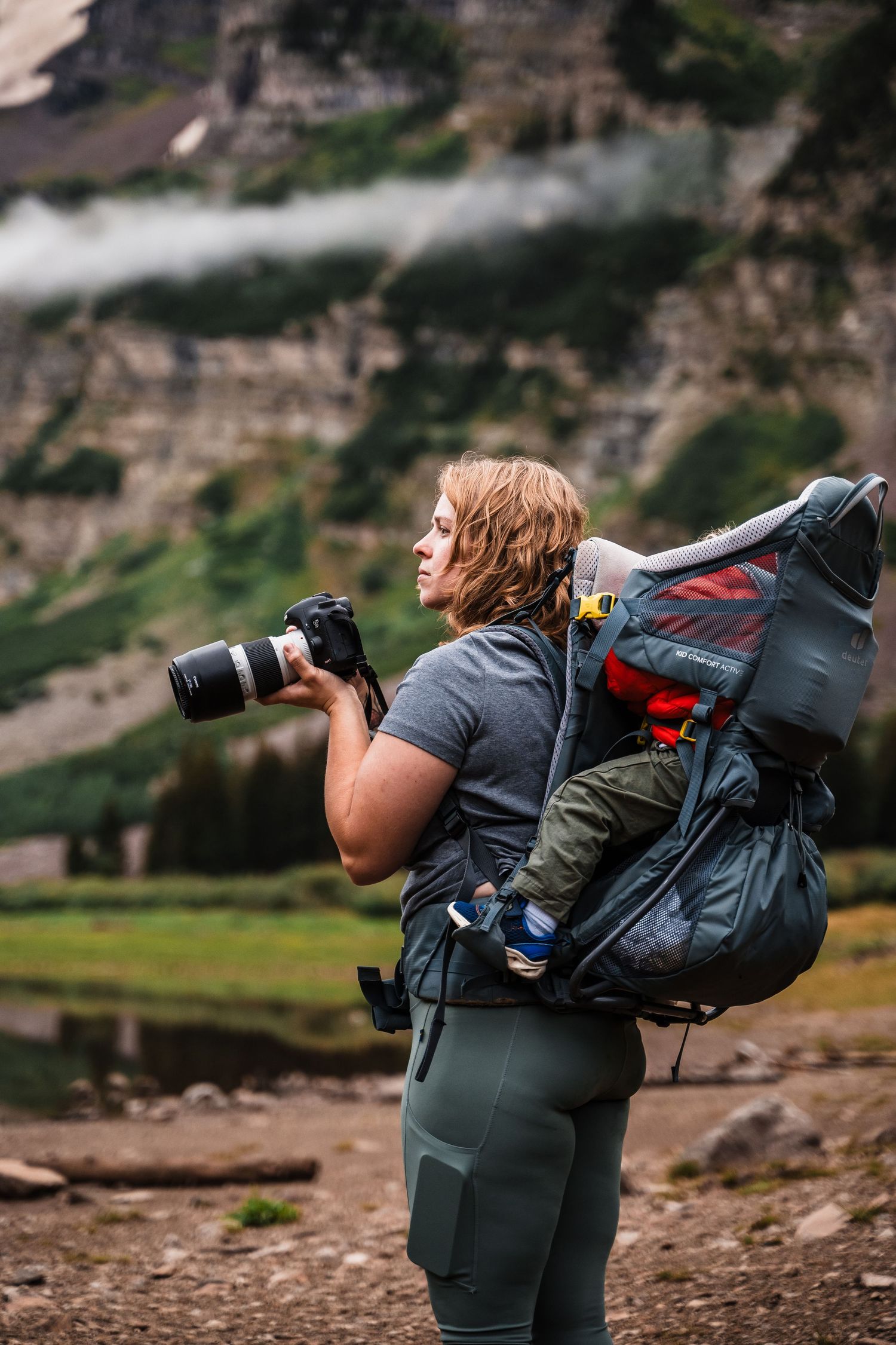 A photographer with camera and backpack captures mountain scenery in an alpine setting.