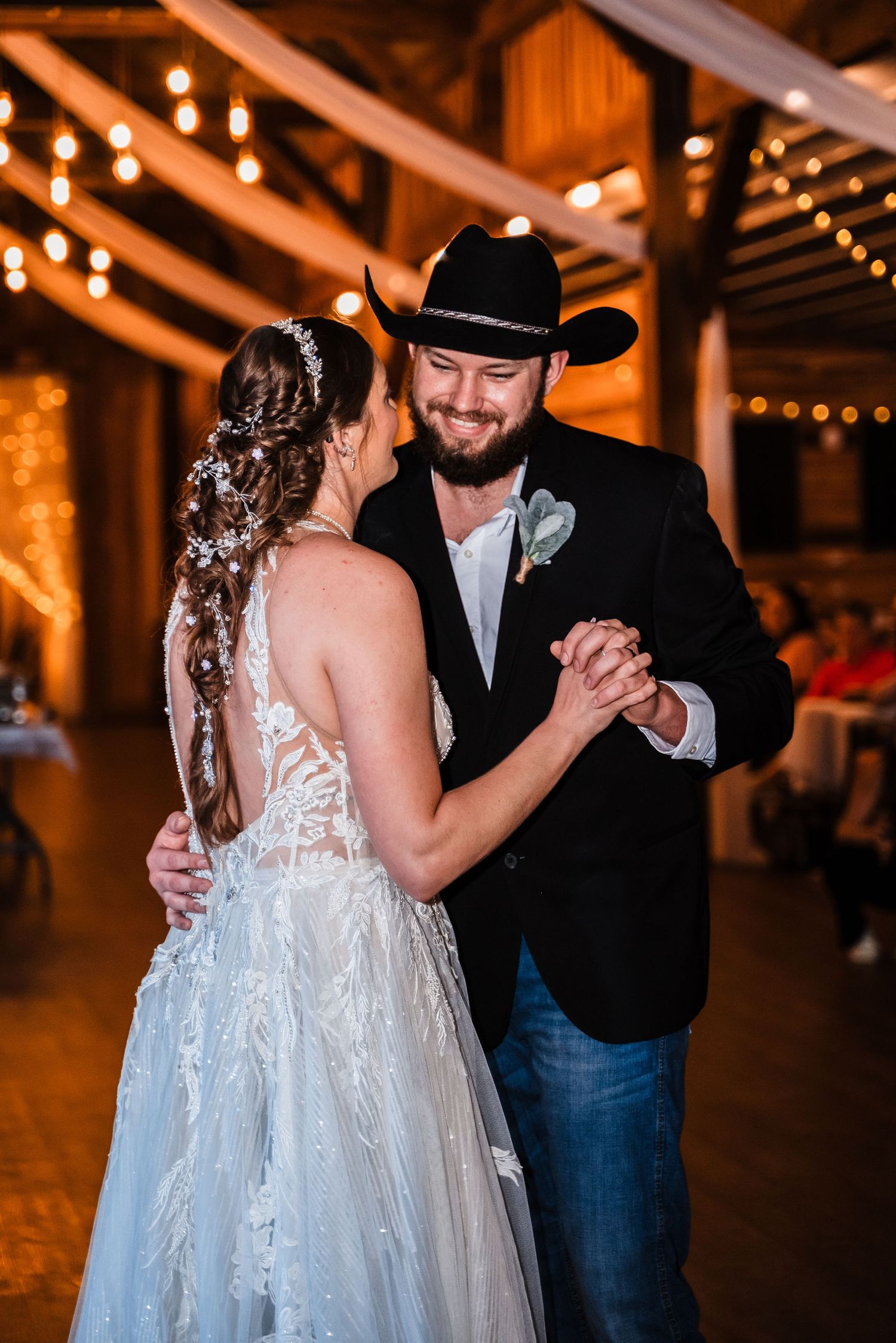 A romantic first dance at a rustic barn wedding venue illuminated by warm string lights.