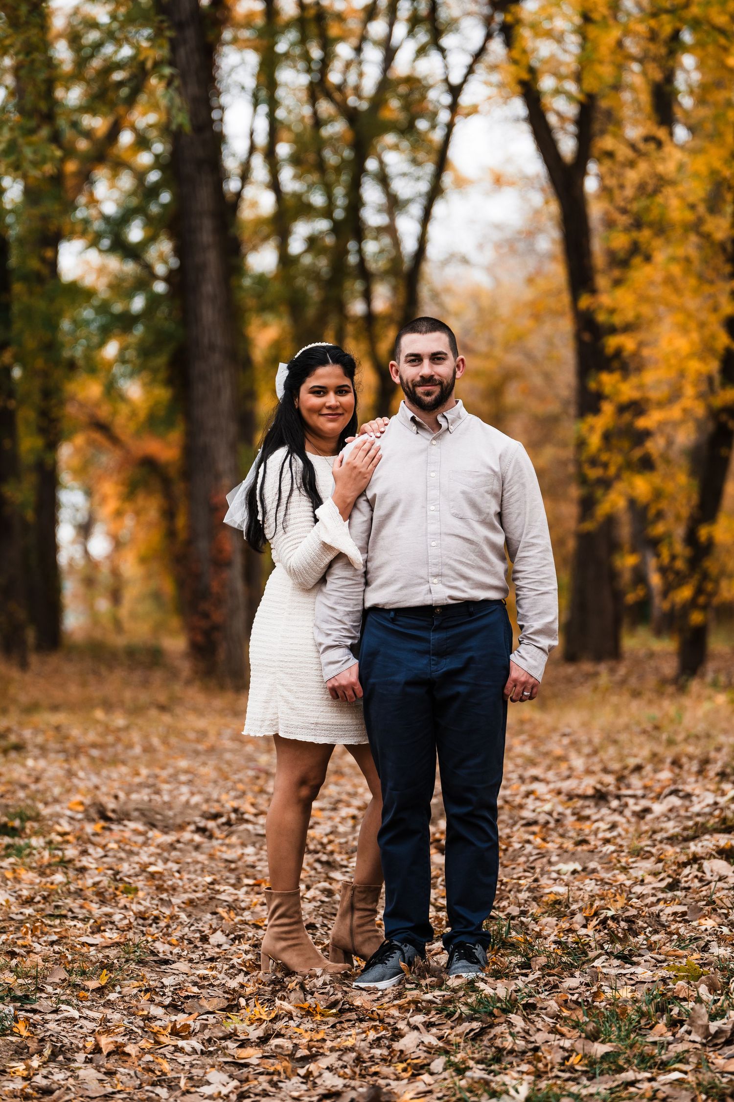 Couple poses together on autumn trail with golden leaves in background.