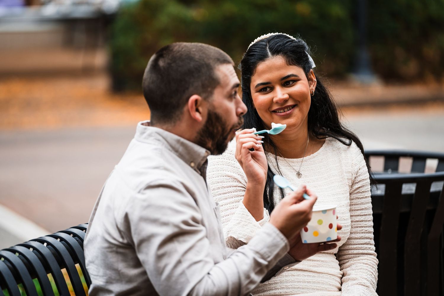 Couple enjoying ice cream together on a park bench in casual attire.