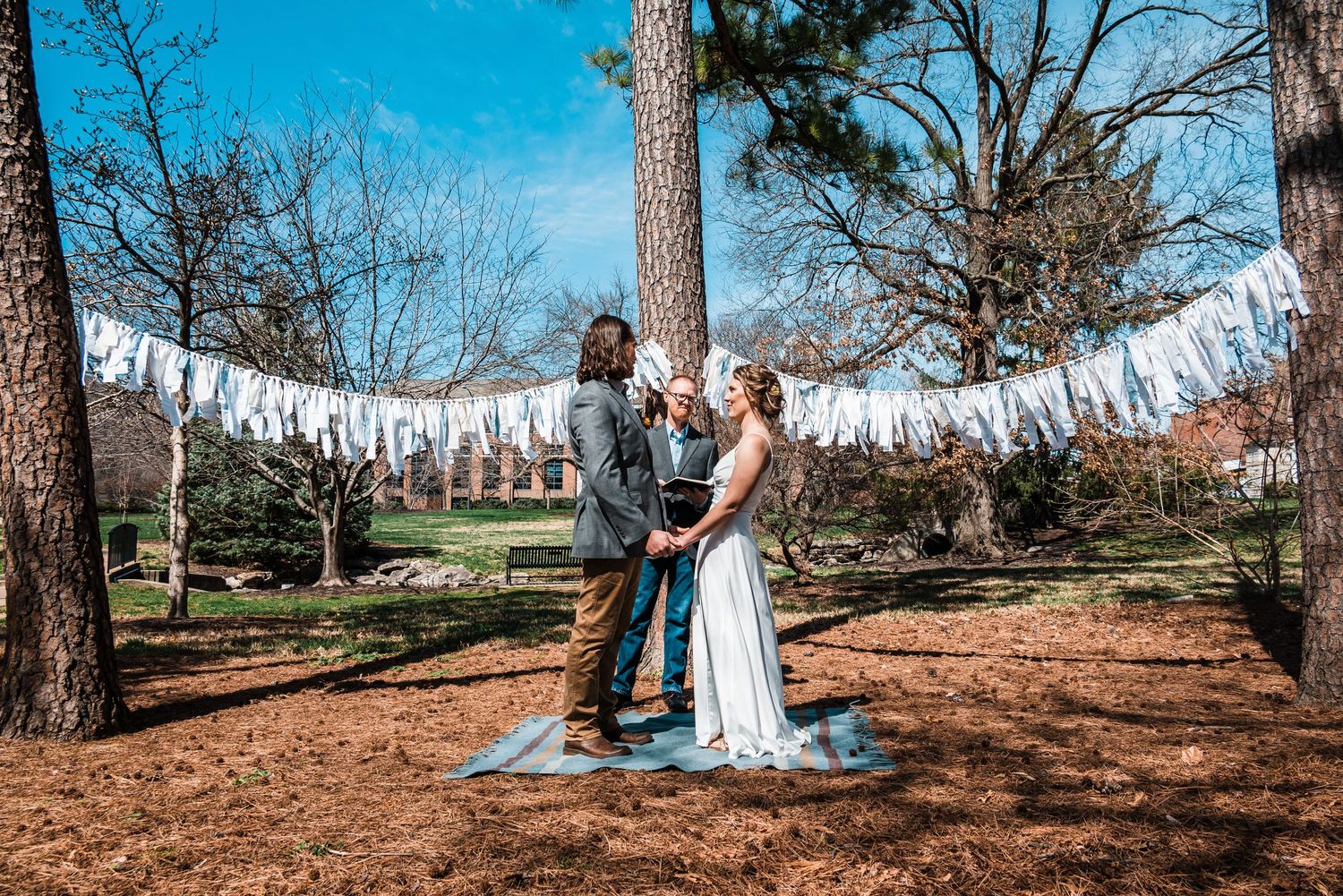 A romantic wedding moment captured under pine trees with white fabric decorations.