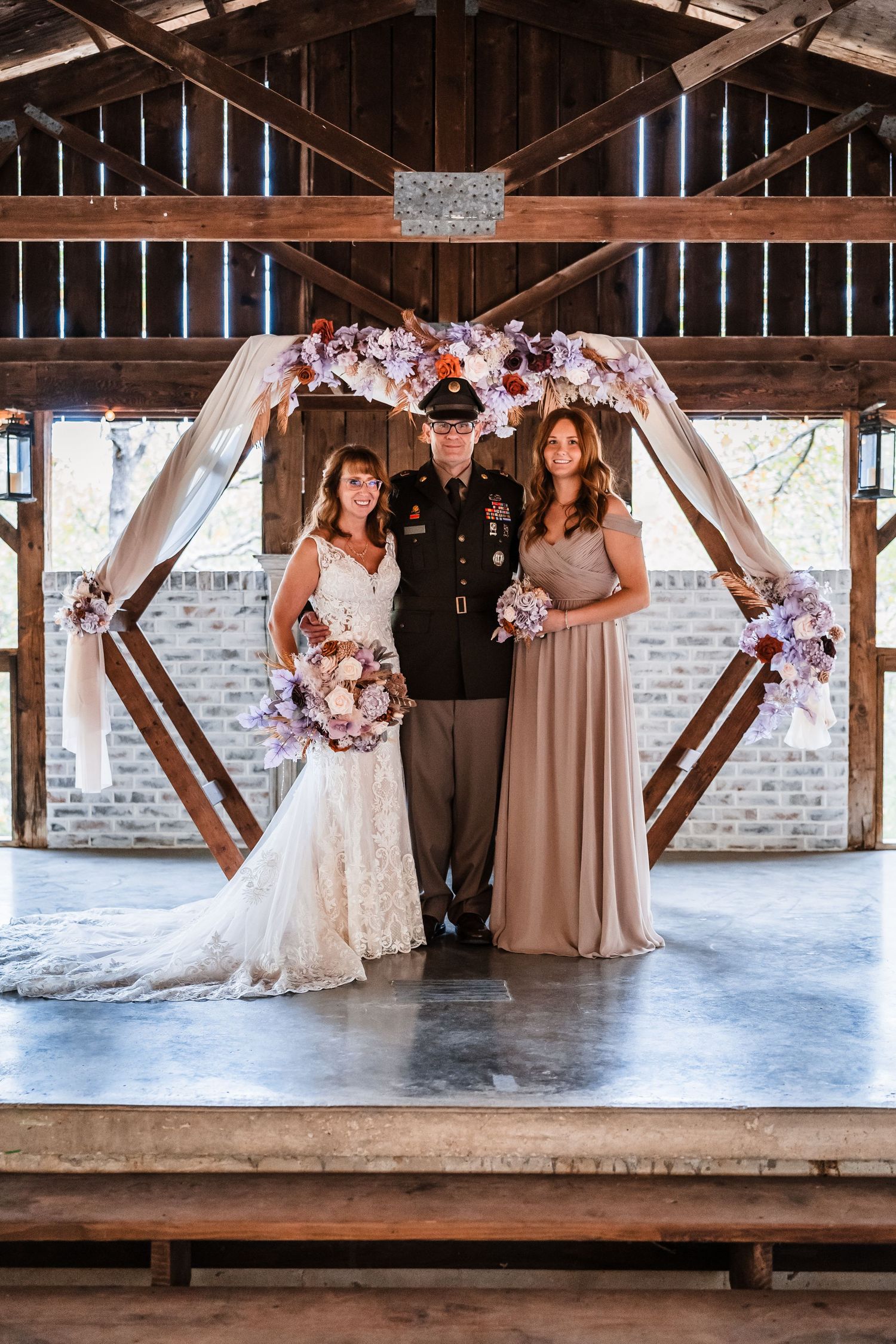 Wedding party poses in a rustic barn venue with exposed beams and brick walls.