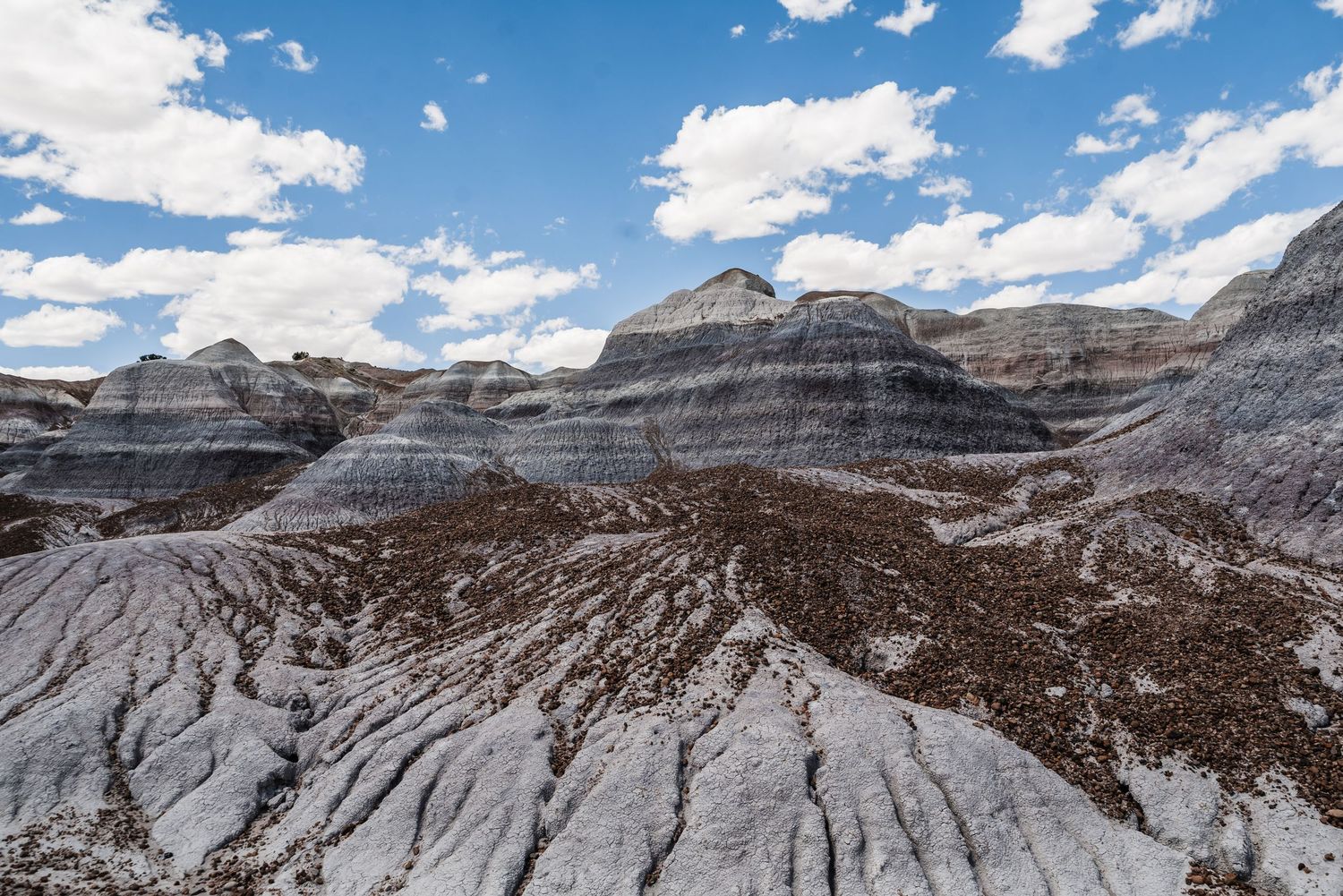 Dramatic layered rock formations under blue sky with white clouds in desert landscape.