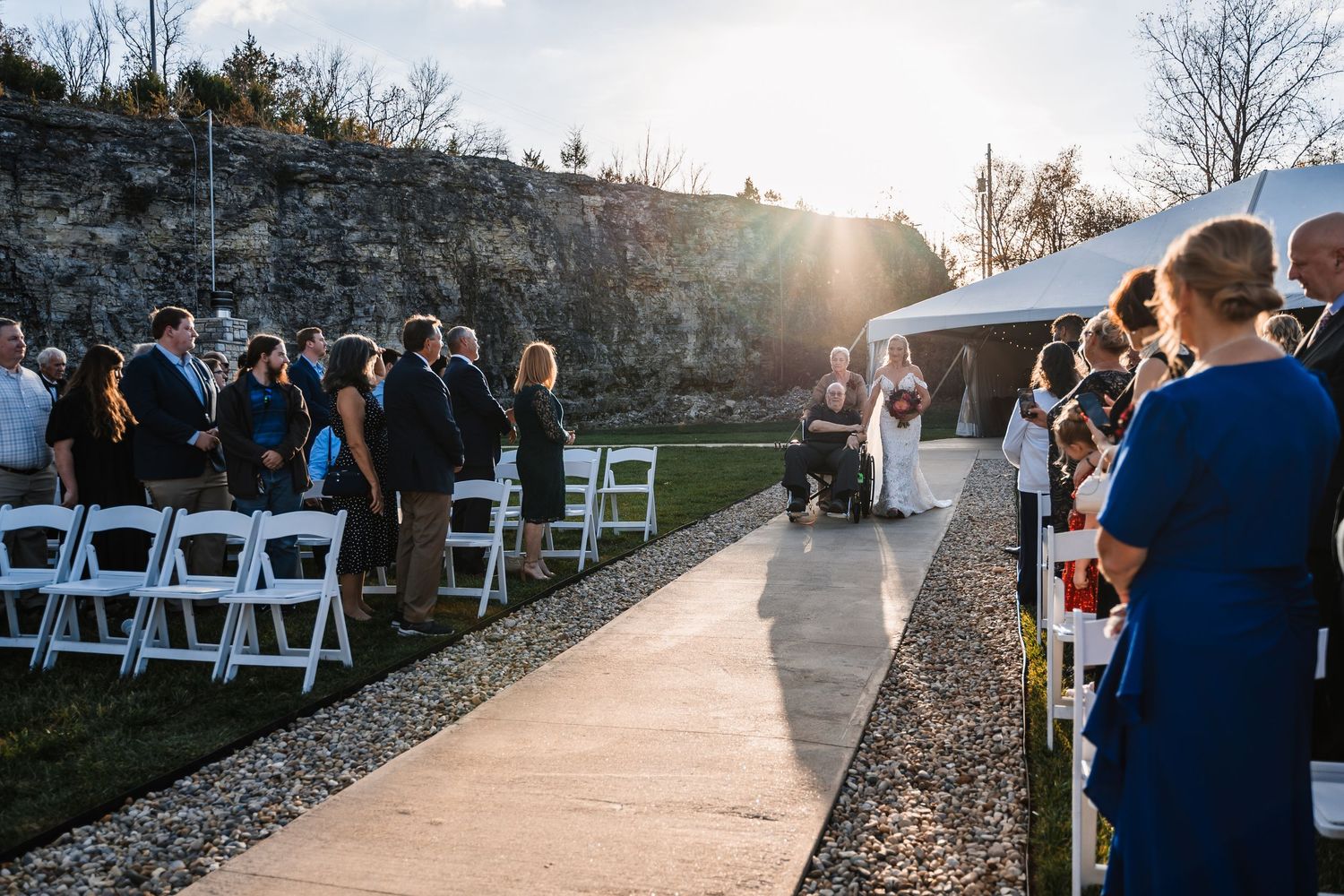 Wedding ceremony setup with white chairs and guests gathered near limestone cliffs at sunset.