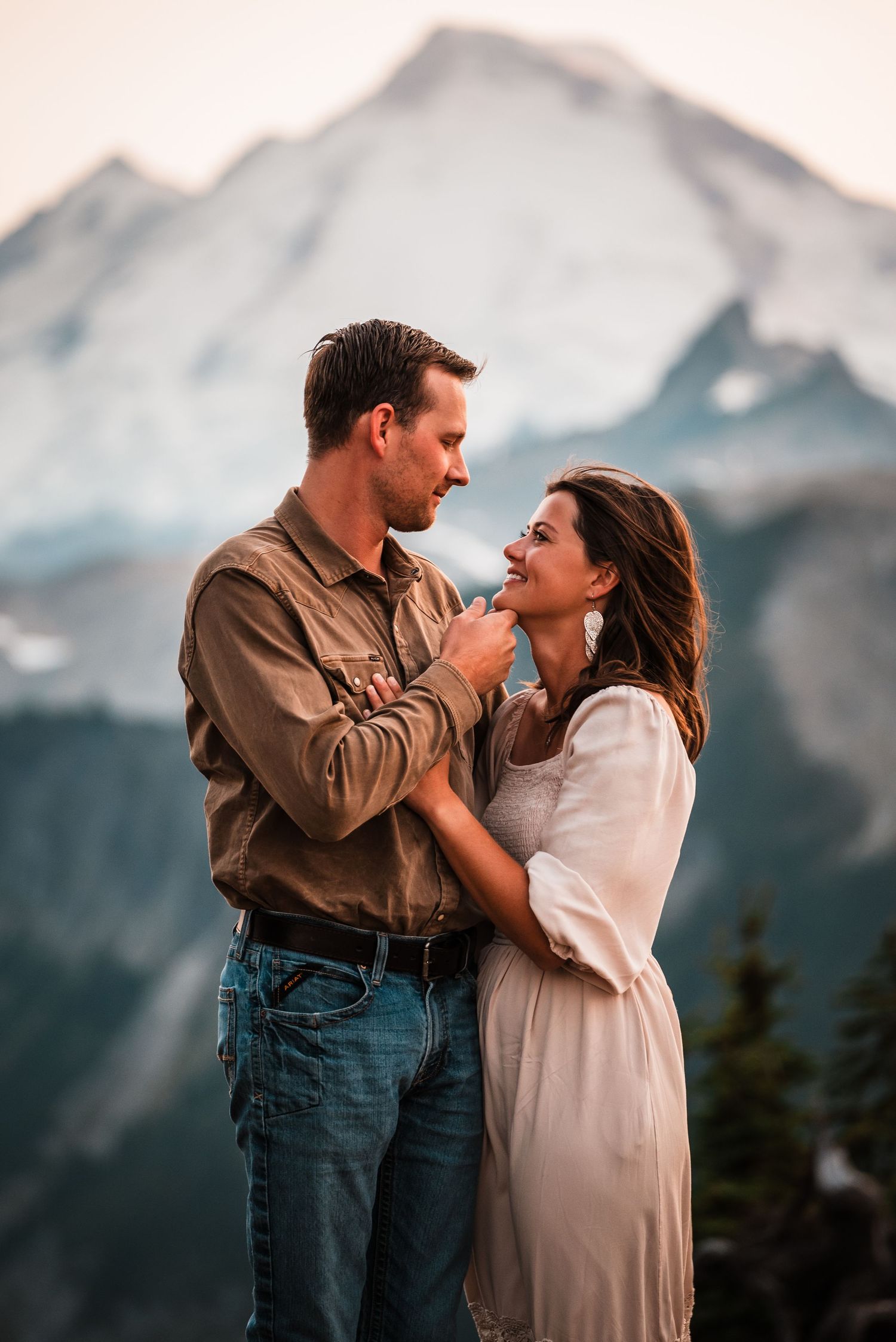 A couple shares an intimate moment against a backdrop of majestic mountain peaks during golden hour.