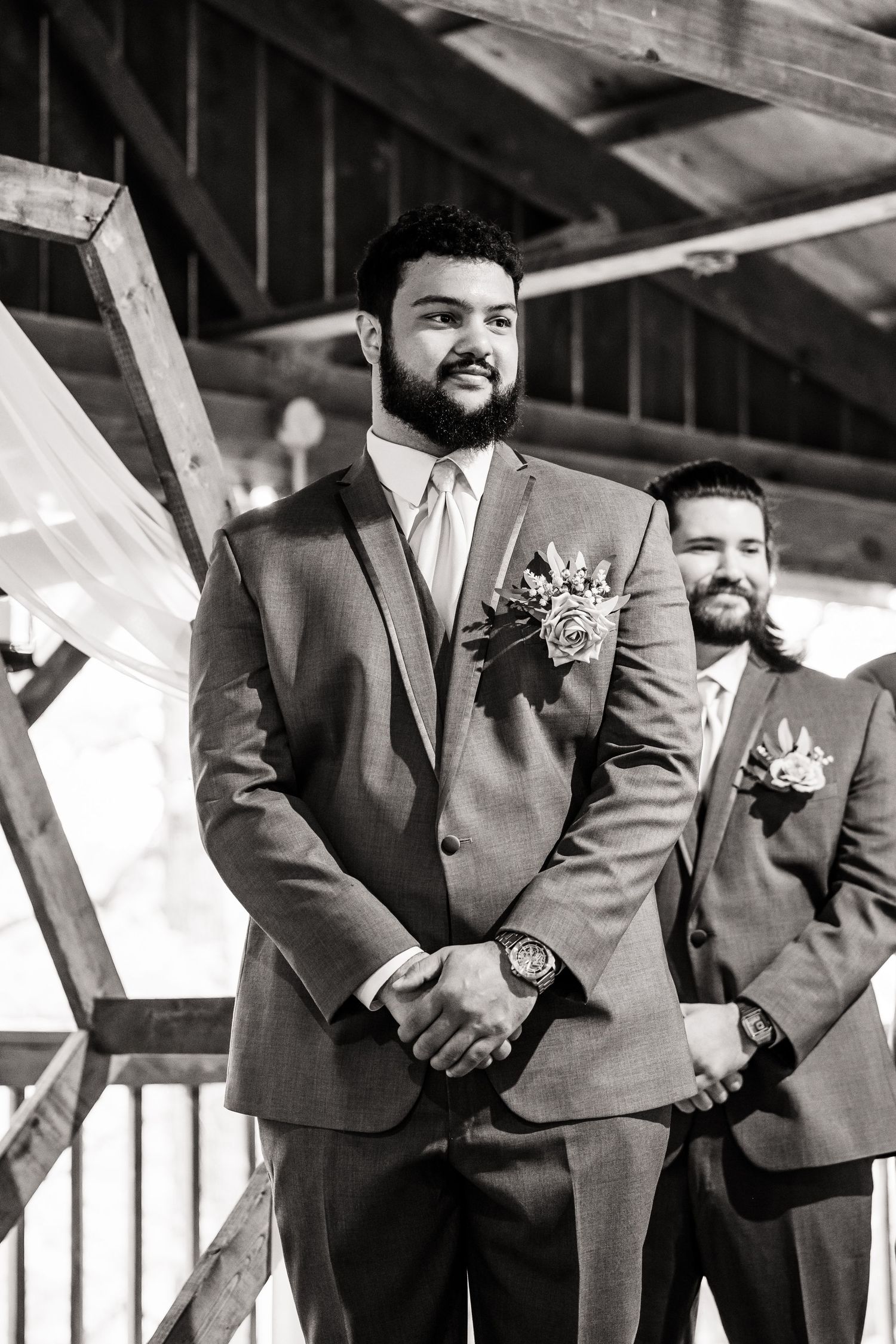 A groom and groomsman stand at a rustic wooden altar during a wedding ceremony.