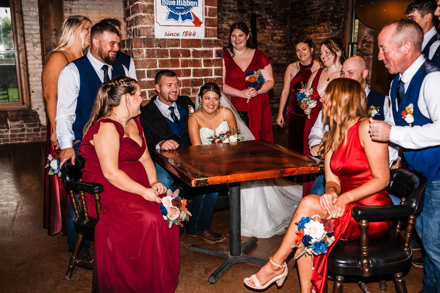 Wedding reception celebration with guests in red dresses dancing in front of exposed brick walls.
