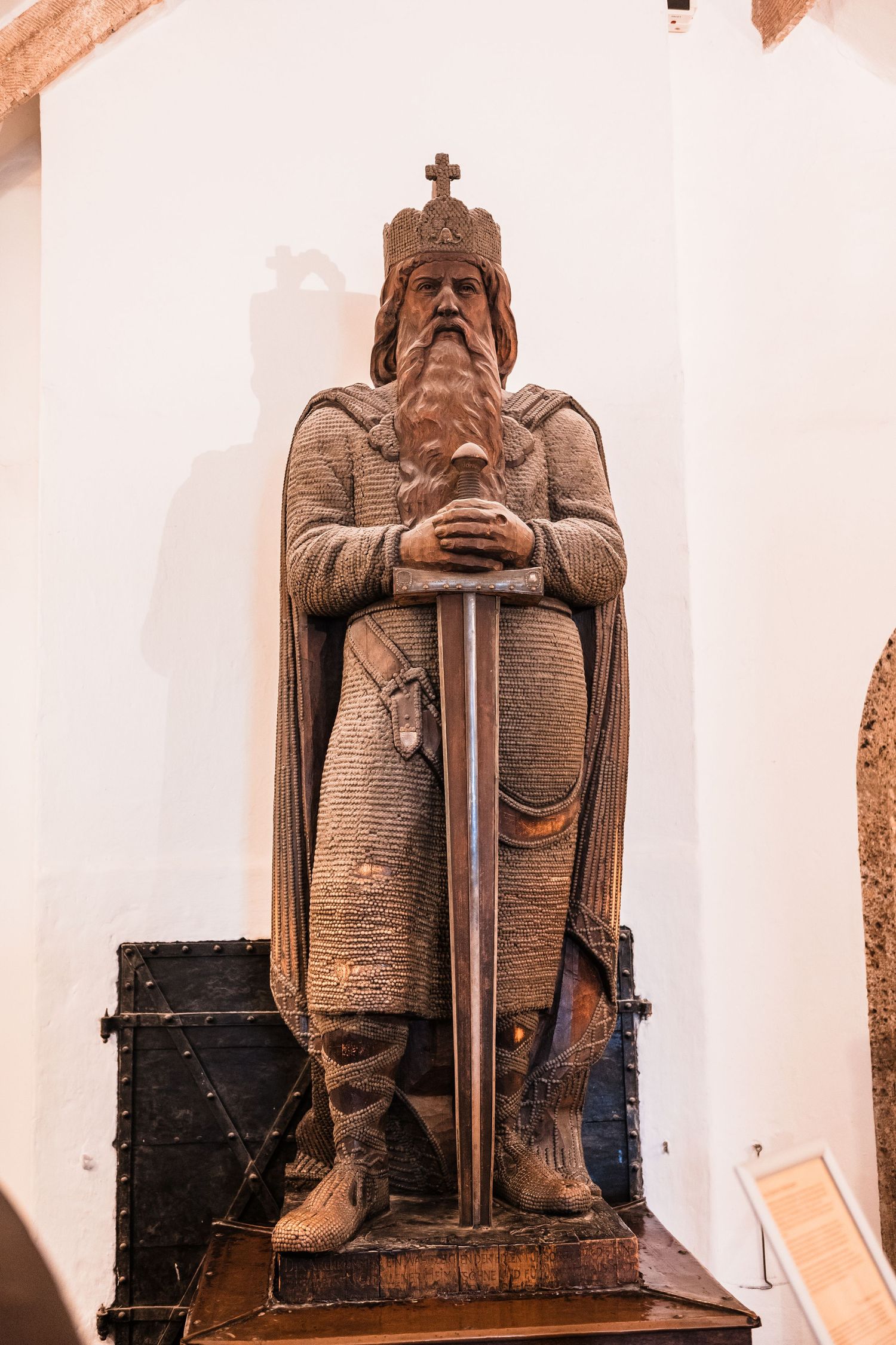 Ancient stone statue of a medieval king or noble figure wearing a crown and holding a sword in a regal pose.