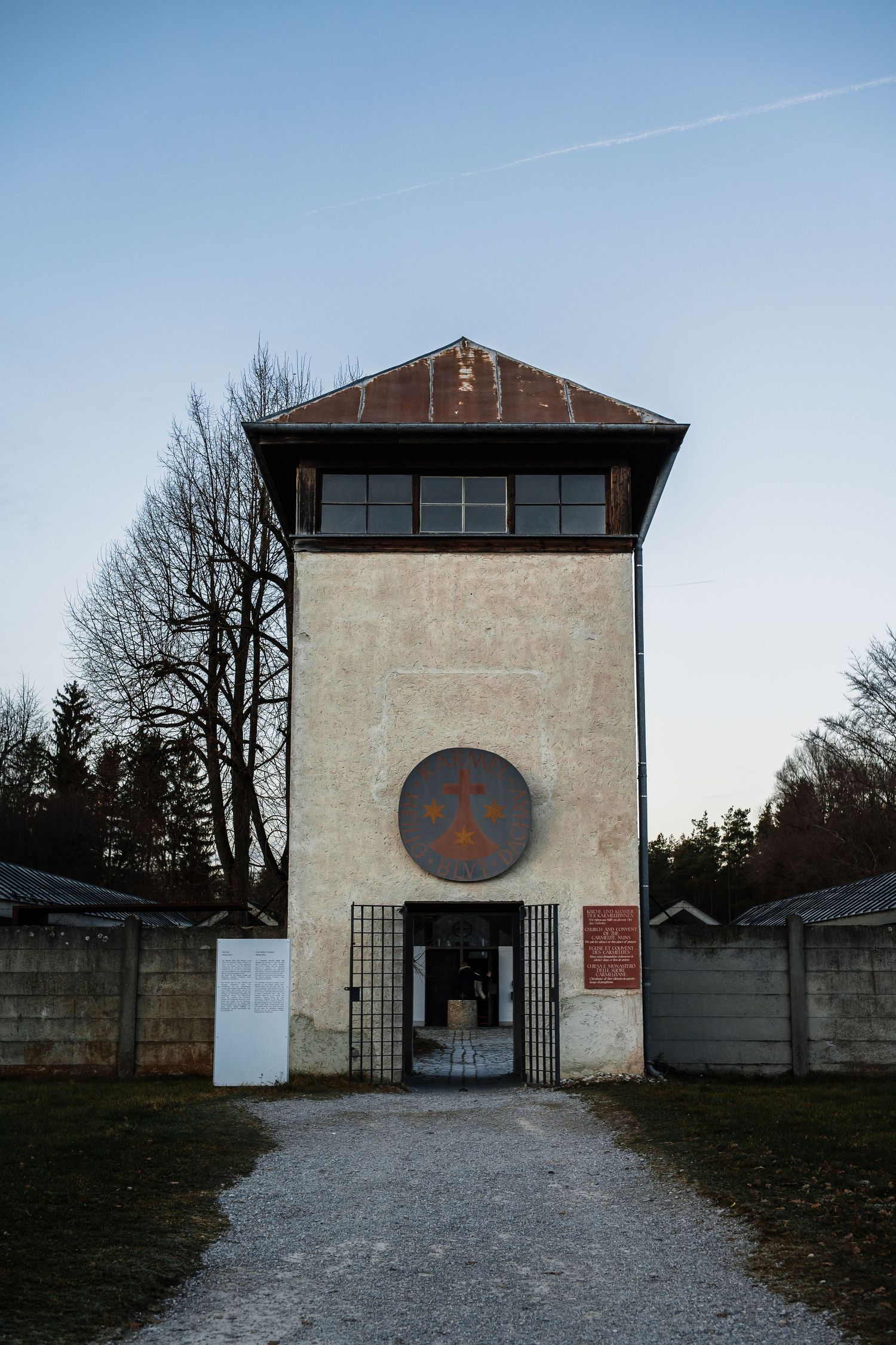 Historic entrance gate to the Dachau concentration camp memorial site with gravel path leading to stone building.