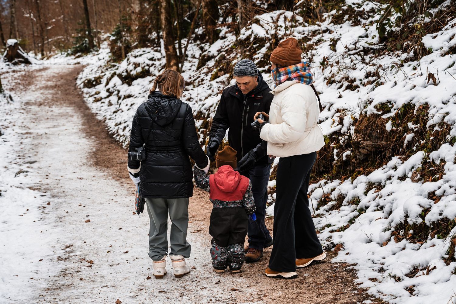 A group of hikers walk along a snowy mountain trail with steep rock walls on either side.