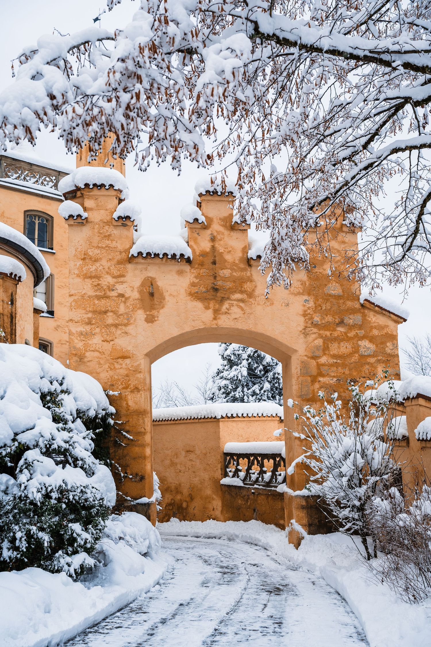 Snow-covered stone archway and path leading through a medieval castle gate in warm orange tones during winter.
