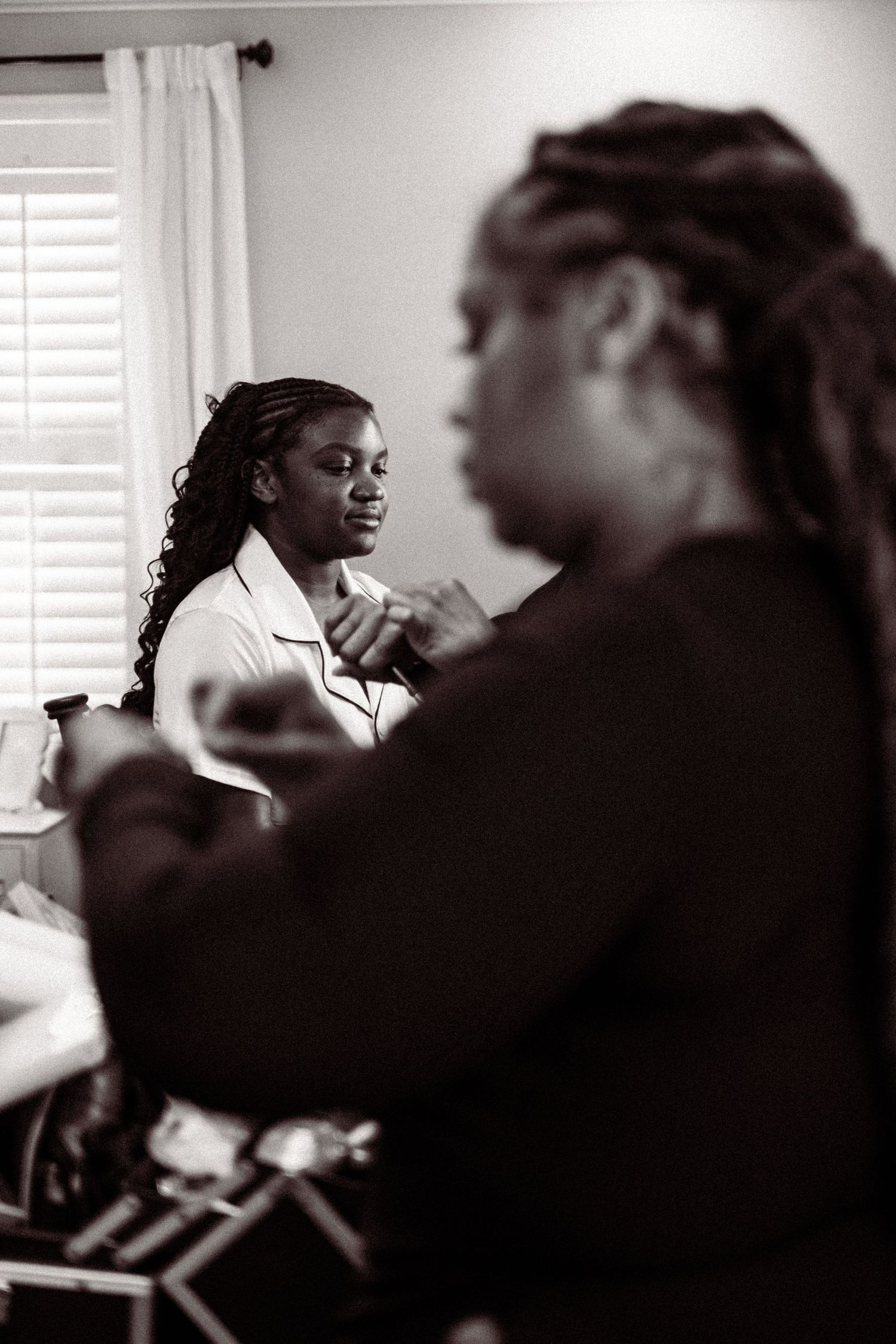 Black and white photo of a bride getting ready with her bridesmaid in a bright room.