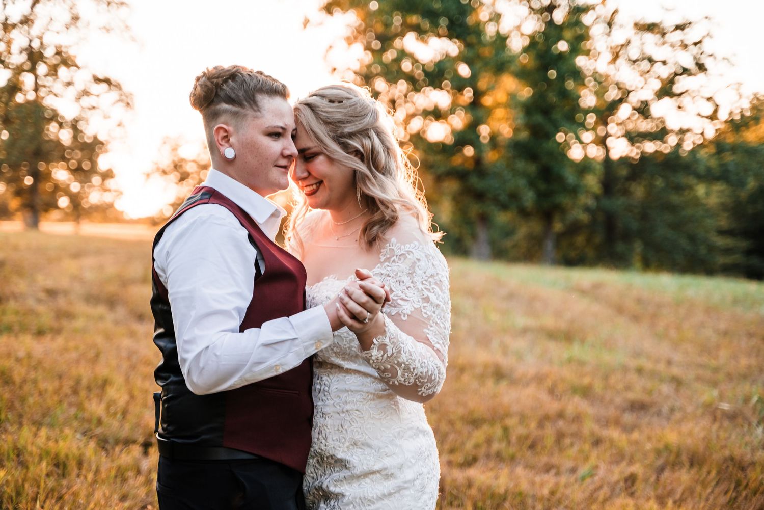 Newlyweds sharing an intimate moment in a sunlit meadow during golden hour.