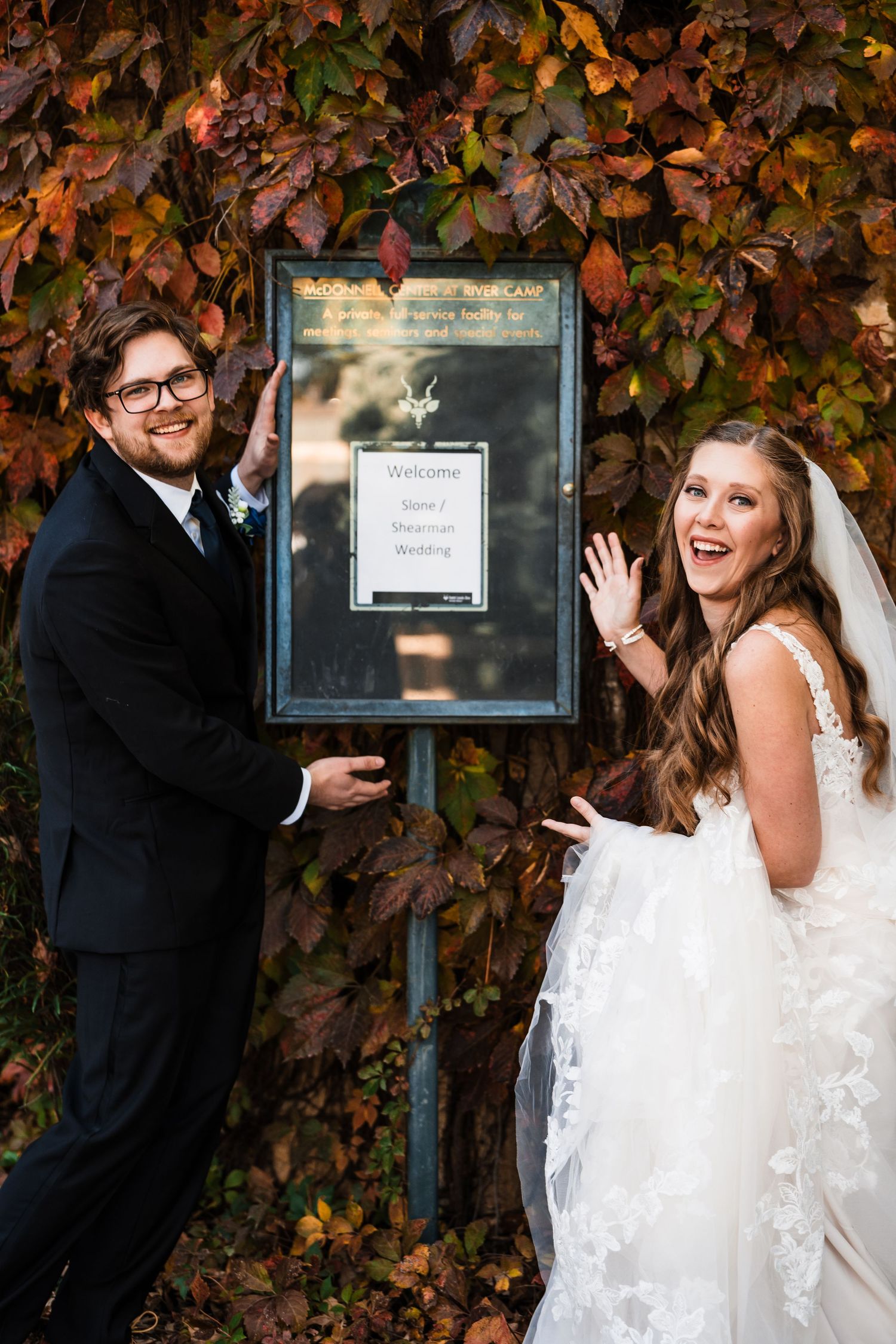 Couple posing playfully by sign surrounded by autumn ivy.