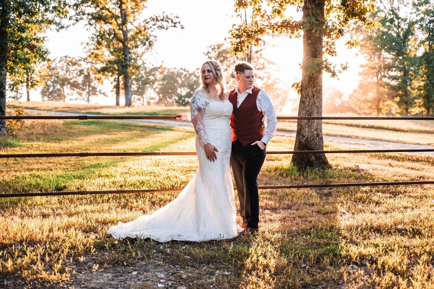 A wedding couple poses together in an autumn field with golden sunlight filtering through trees.